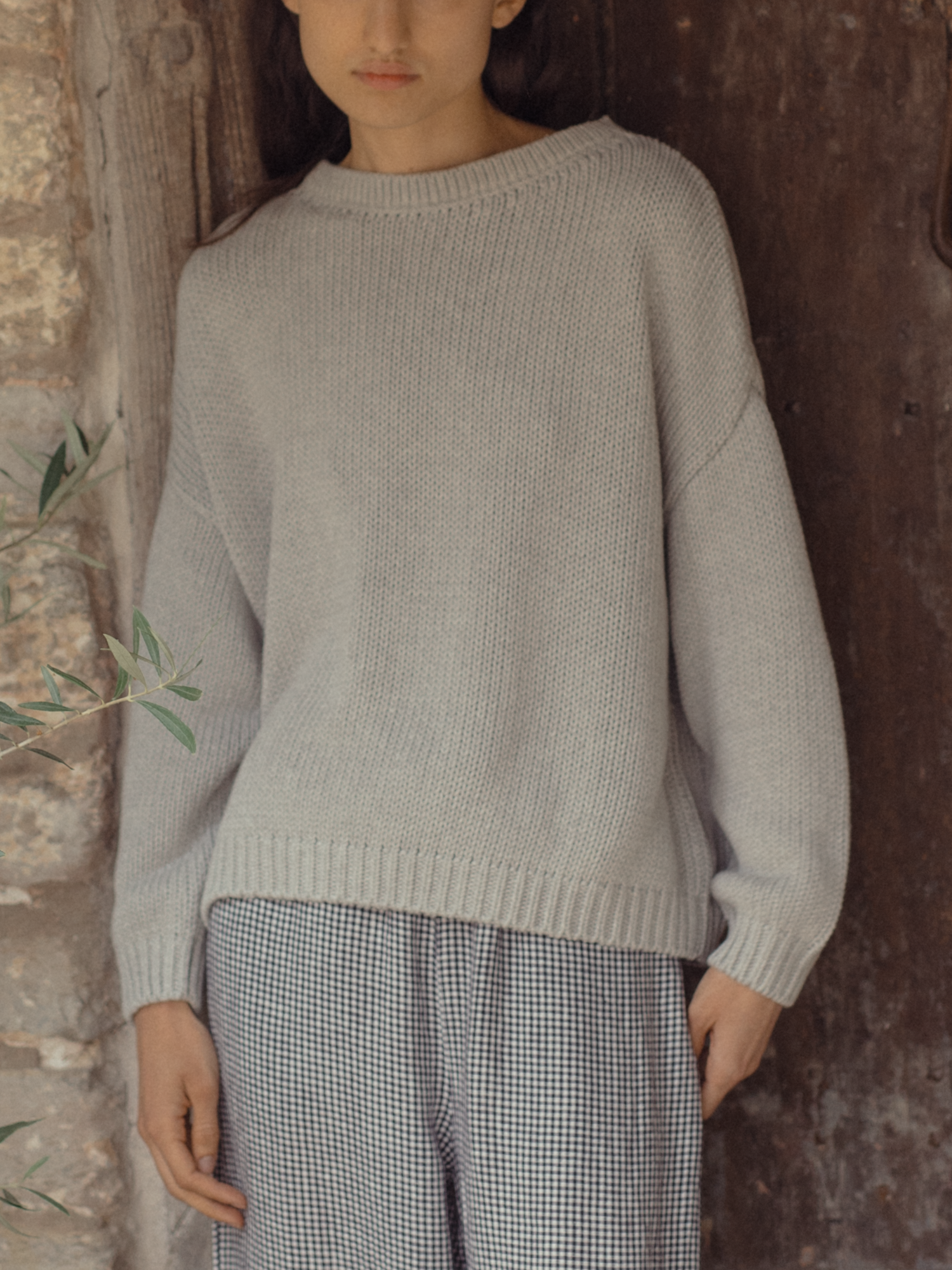 Model wearing the Townes Pullover in Pebble by Gillian Stevens, front view against a stone wall