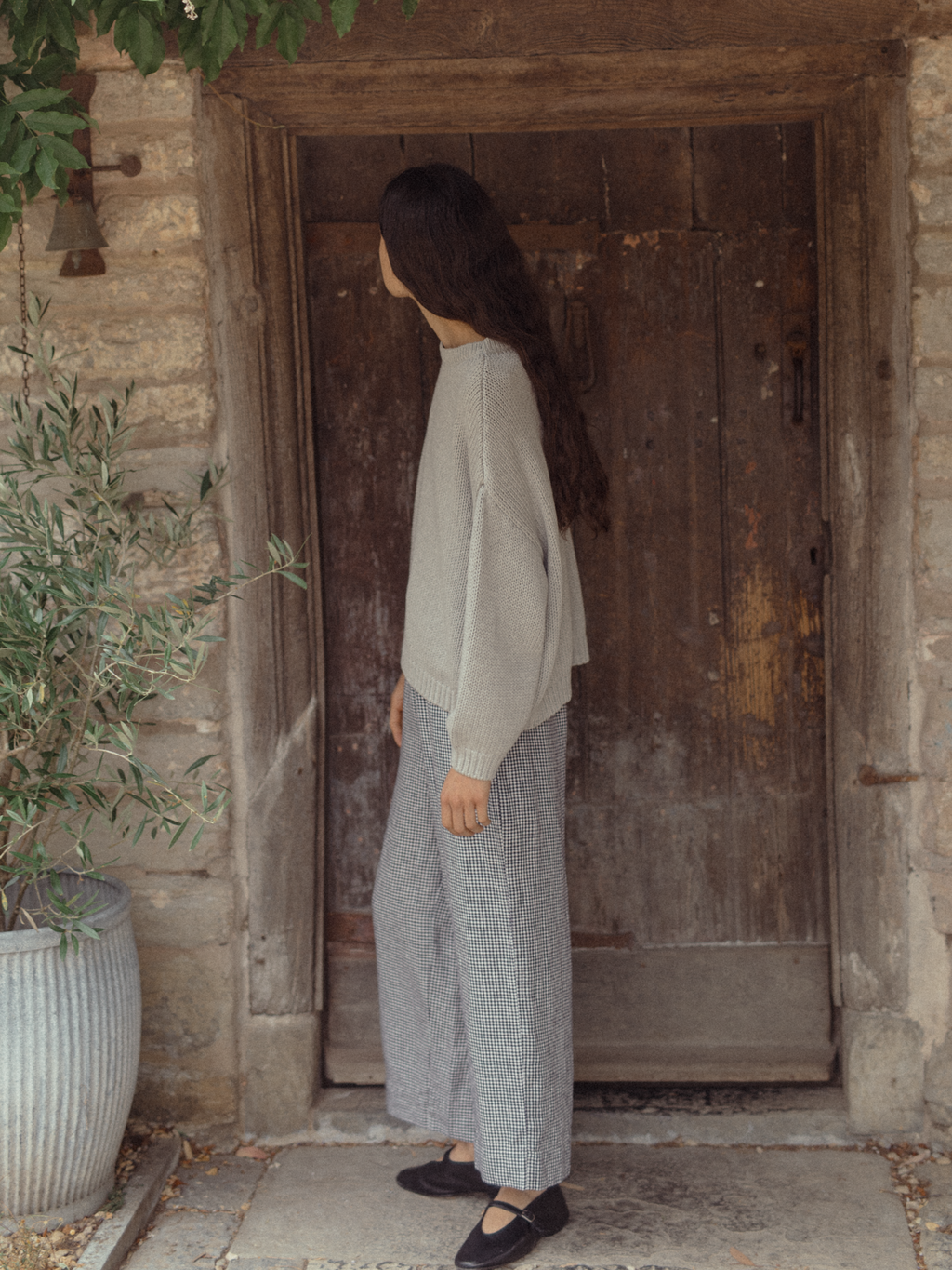 Model wearing the Townes Pullover in Pebble by Gillian Stevens, side view at a rustic stone doorway