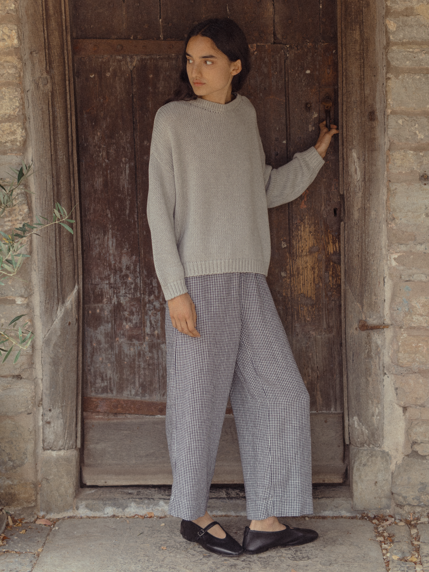 Model wearing the Townes Pullover in Pebble by Gillian Stevens, full-length front view at a rustic stone doorway