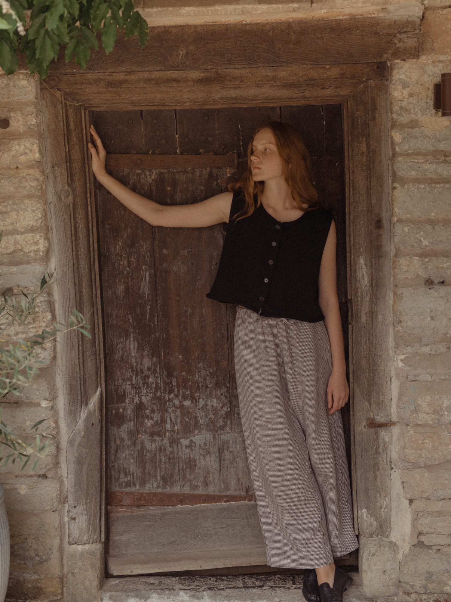 Model in the Olive Pant in Espresso Gingham by Gillian Stevens, front view in a rustic stone doorway