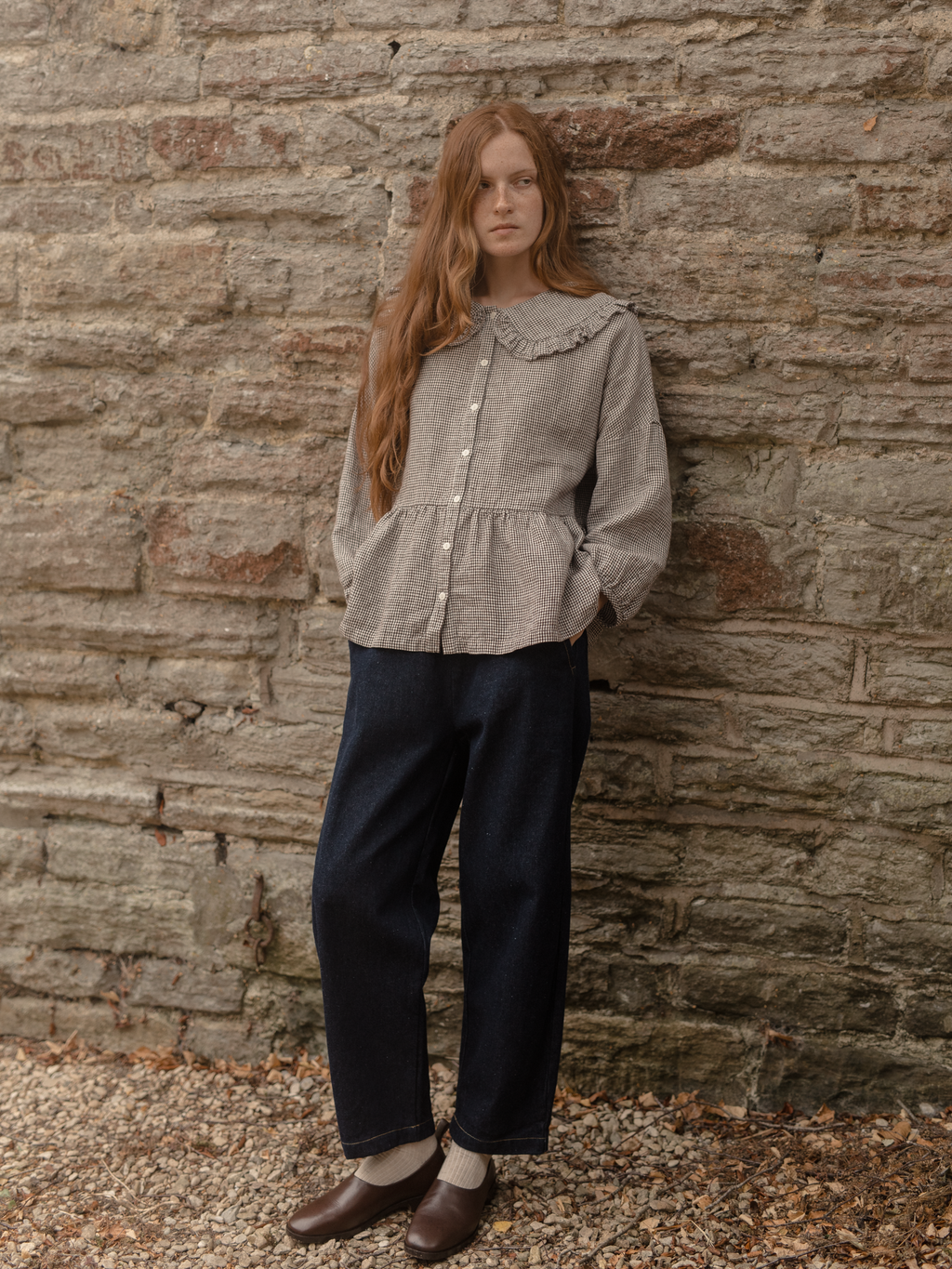 Model wearing the Winsley Blouse in Espresso Gingham by Gillian Stevens, full-length front view against a stone wall