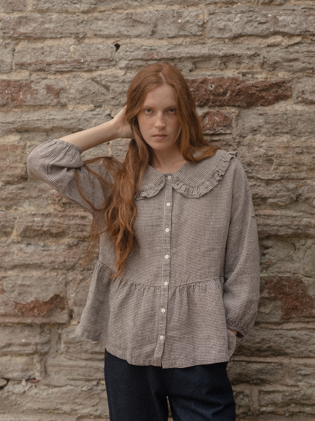 Model wearing the Winsley Blouse in Espresso Gingham by Gillian Stevens, front view against a stone wall