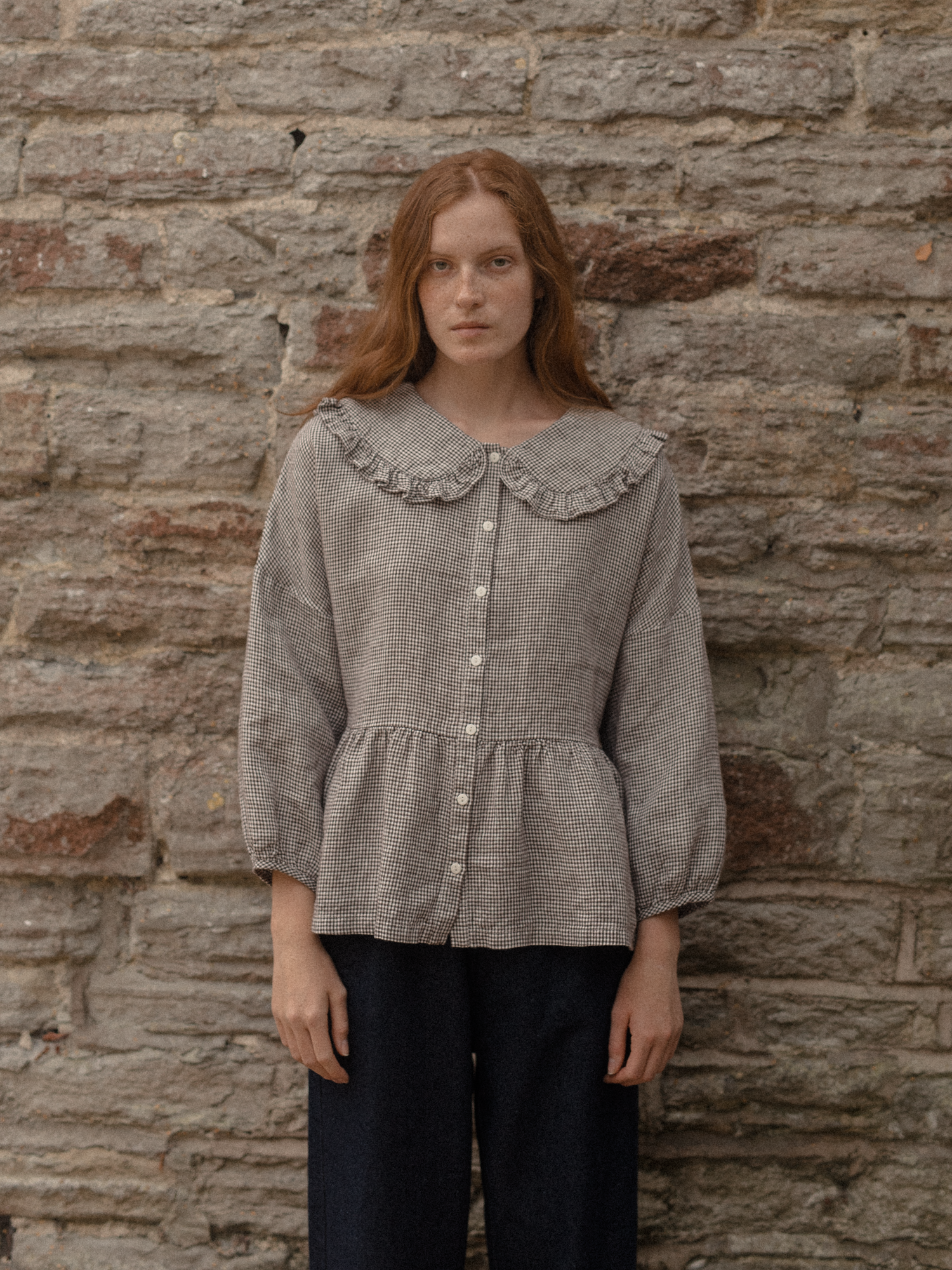 Model wearing the Winsley Blouse in Espresso Gingham by Gillian Stevens, front view against a stone wall