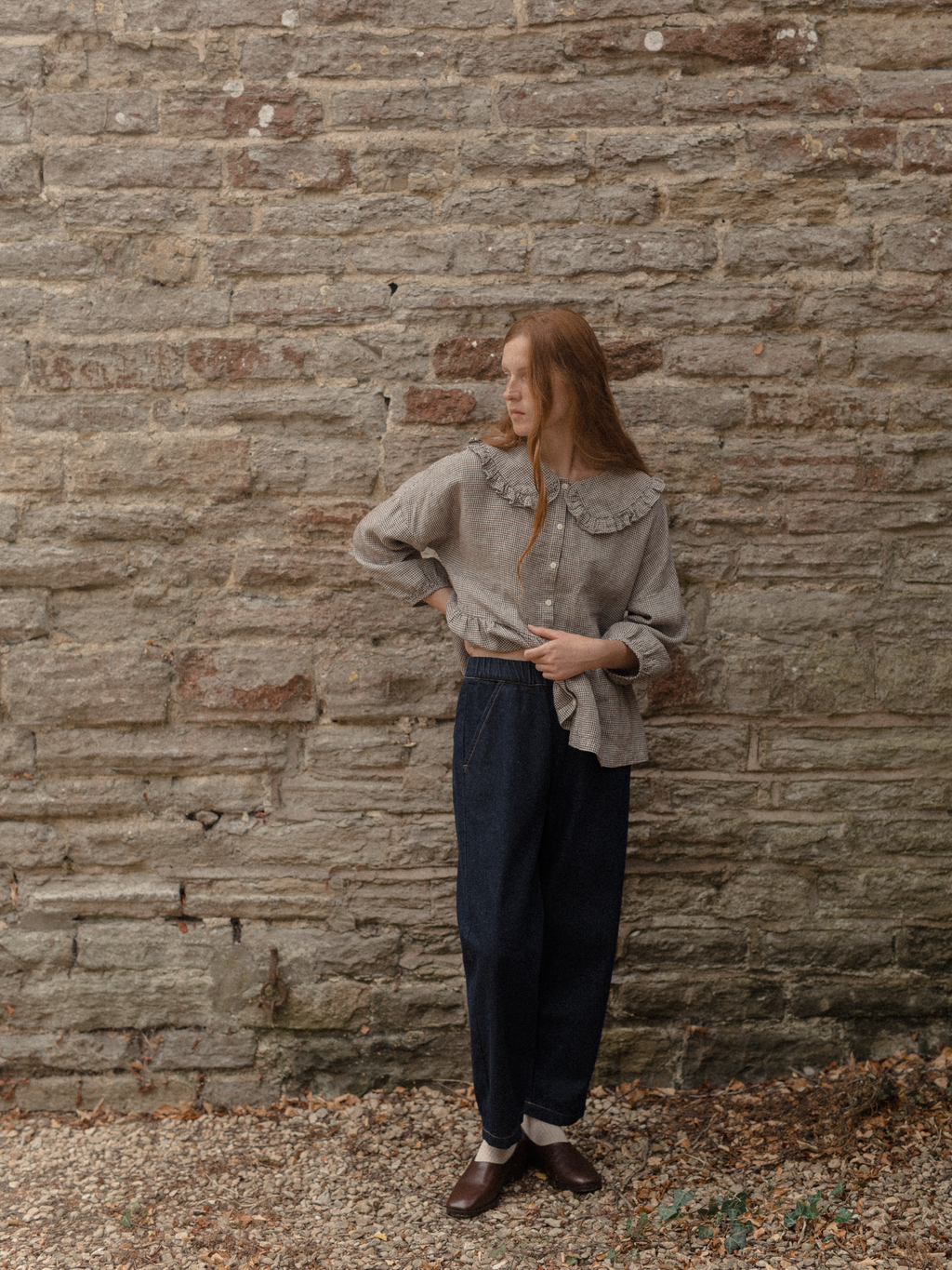 Model wearing the Winsley Blouse in Espresso Gingham by Gillian Stevens, full-length front view against a stone wall