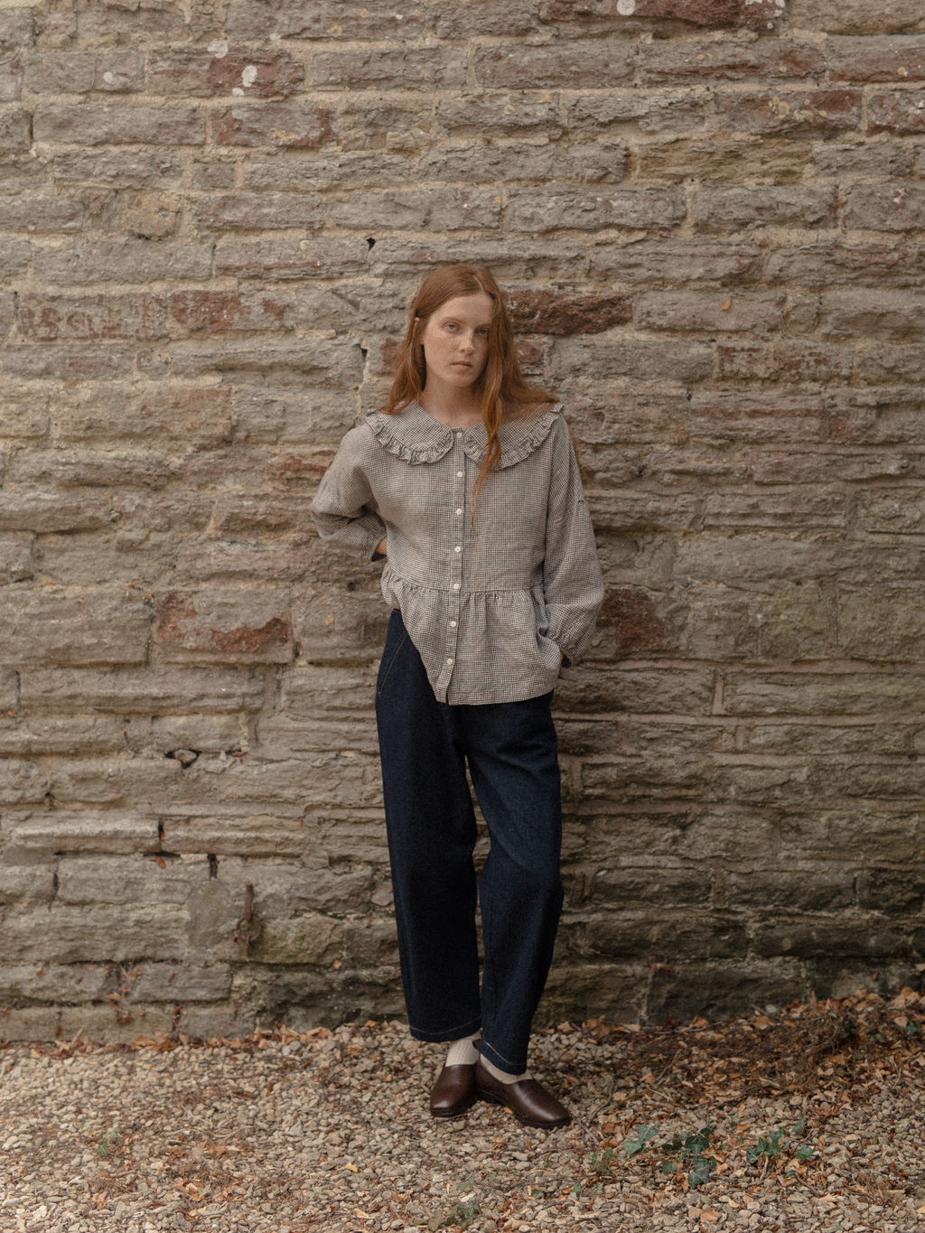 Model wearing the Winsley Blouse in Espresso Gingham by Gillian Stevens, full-length front view against a stone wall