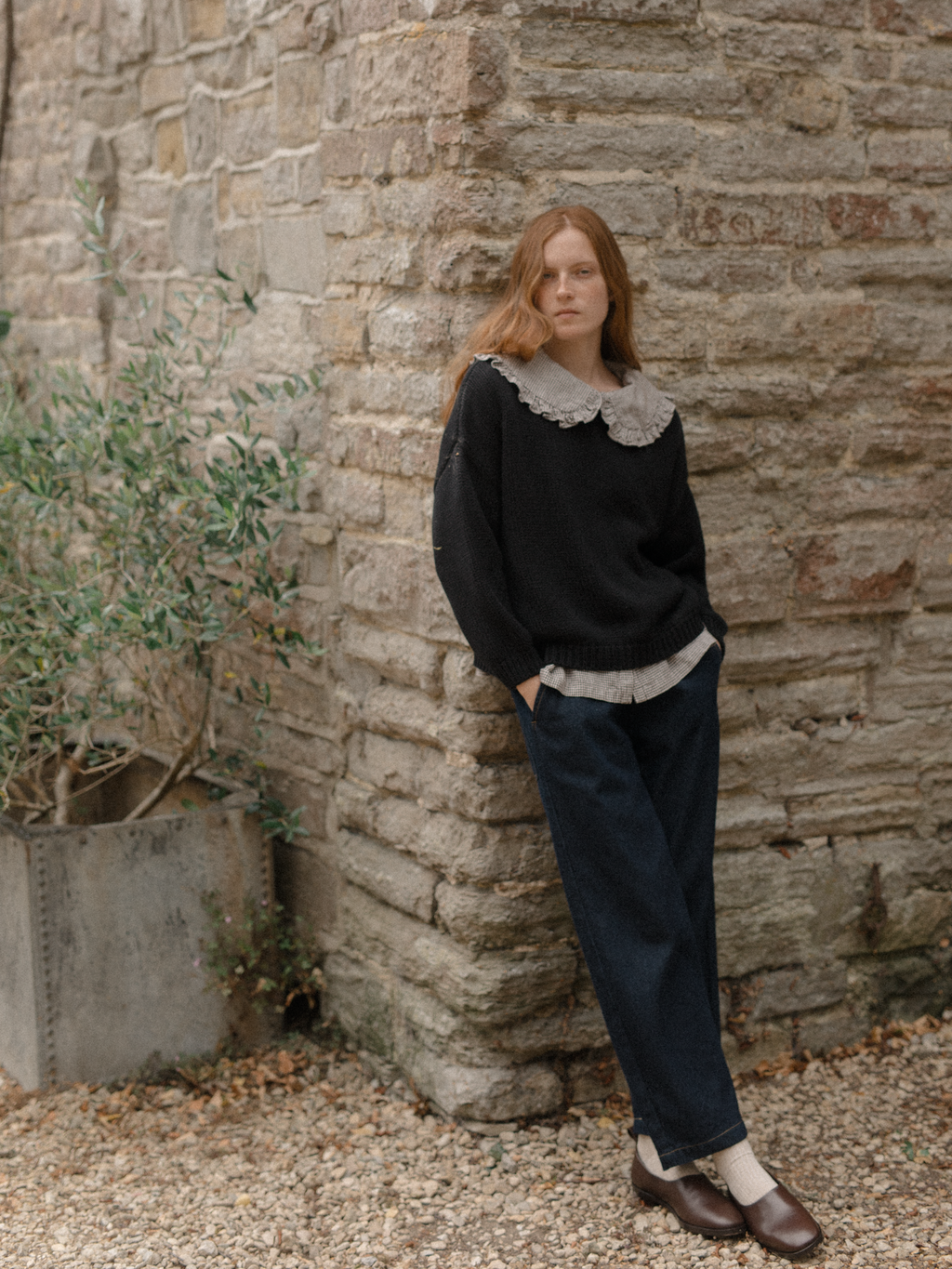 Model wearing the Townes Pullover in Noir by Gillian Stevens, full-length front view against a stone wall