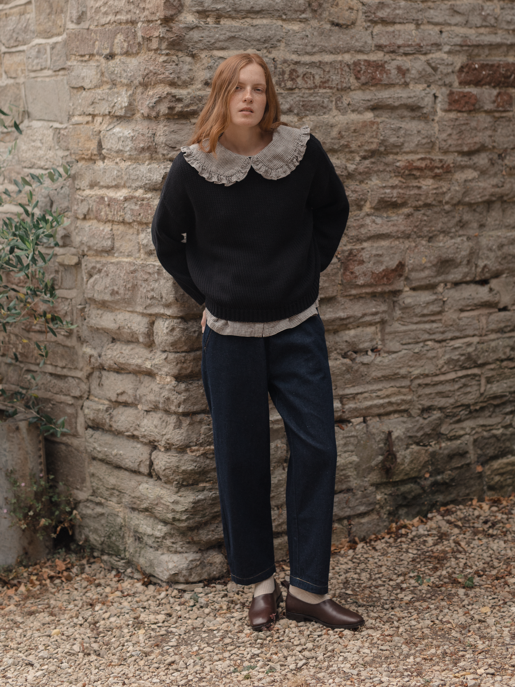 Model wearing the Townes Pullover in Noir by Gillian Stevens, styled with jeans against a stone wall