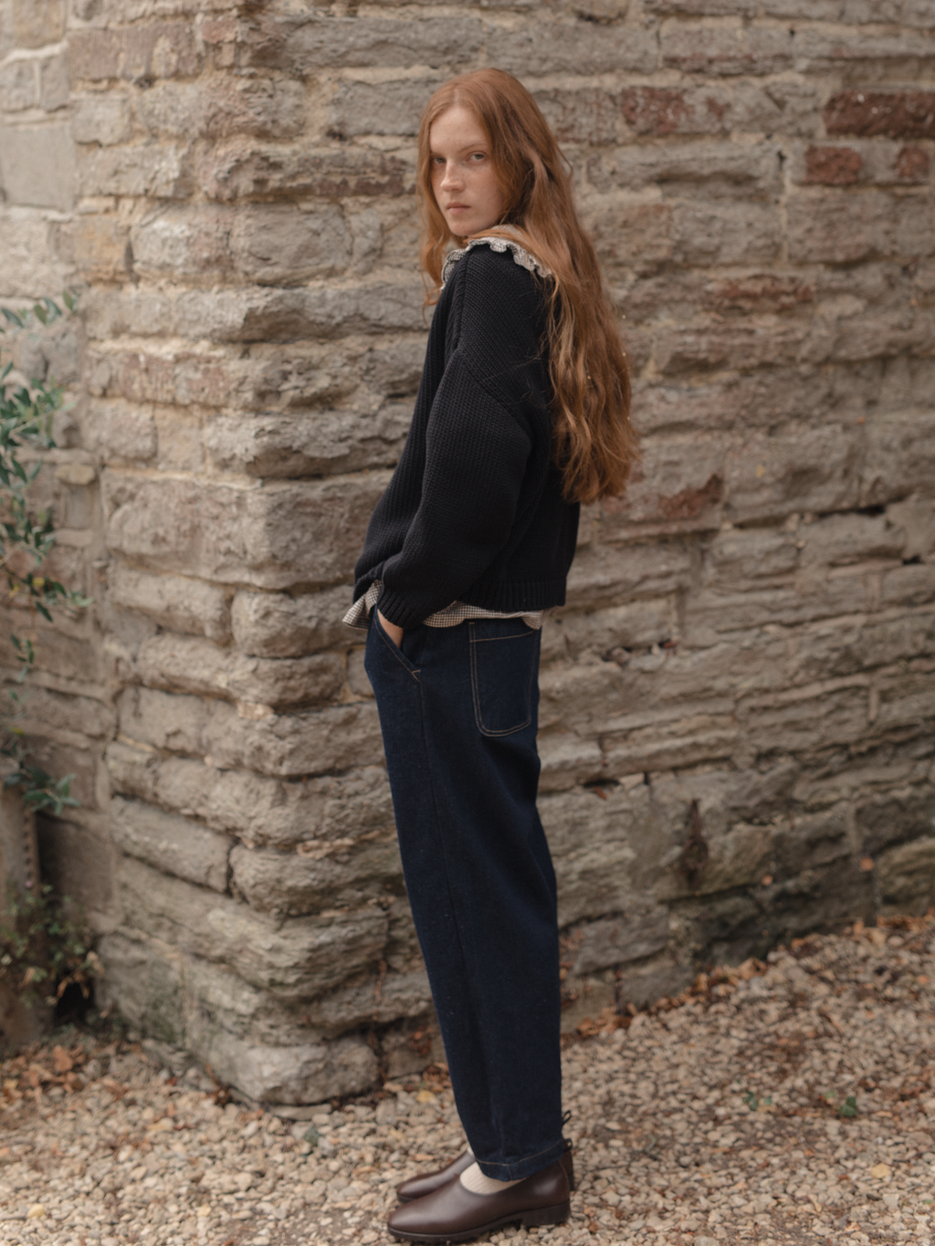 Model wearing the Townes Pullover in Noir by Gillian Stevens, side view against a stone wall