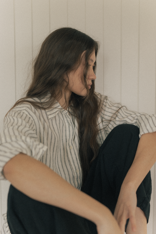 Model wearing the Britta Shirt Linen in Vintage Stripe by Gillian Stevens, seated side profile view