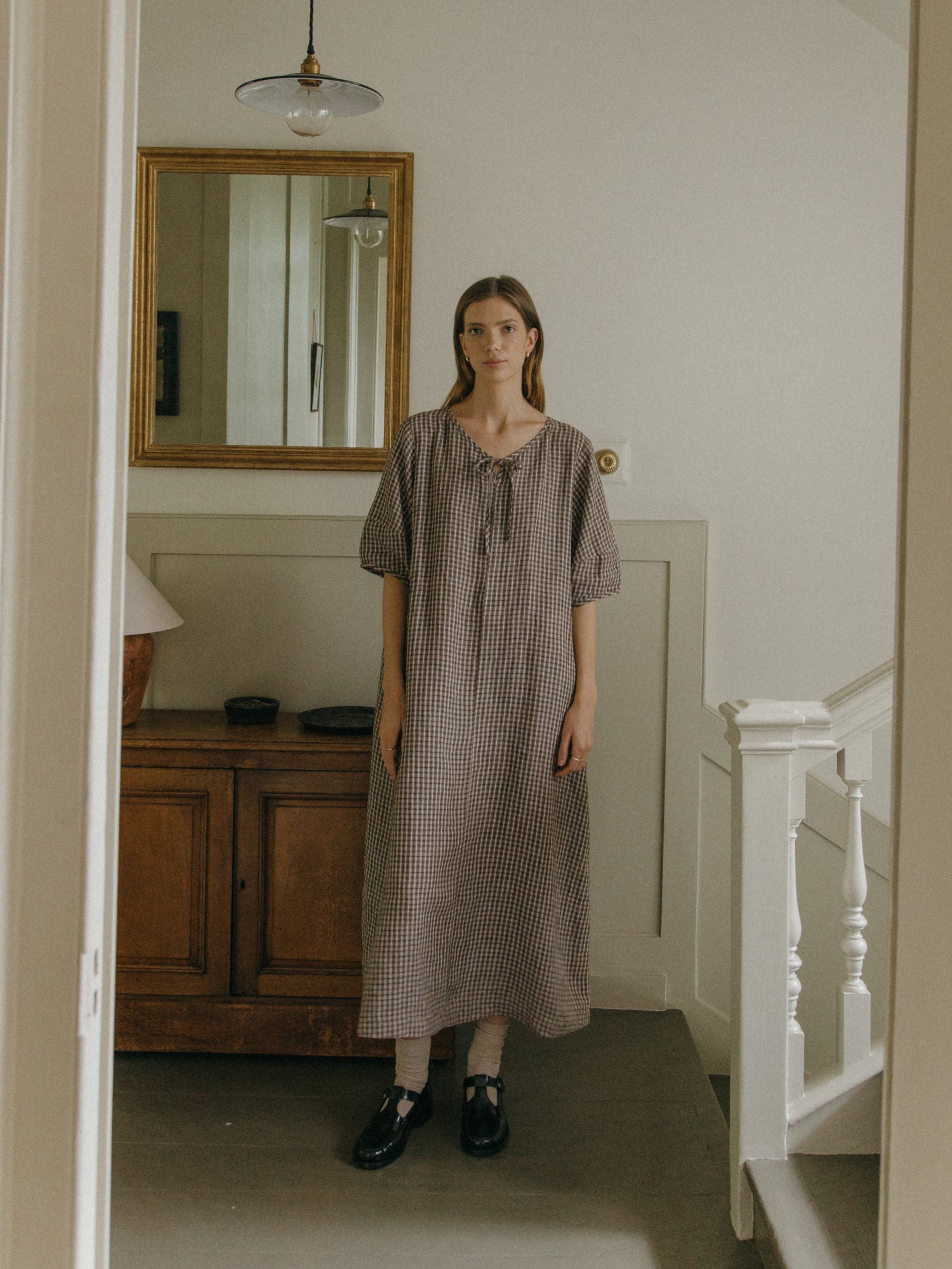 Model wearing the Blair Dress in Chocolate Plaid by Gillian Stevens, full-length front view in a hallway setting
