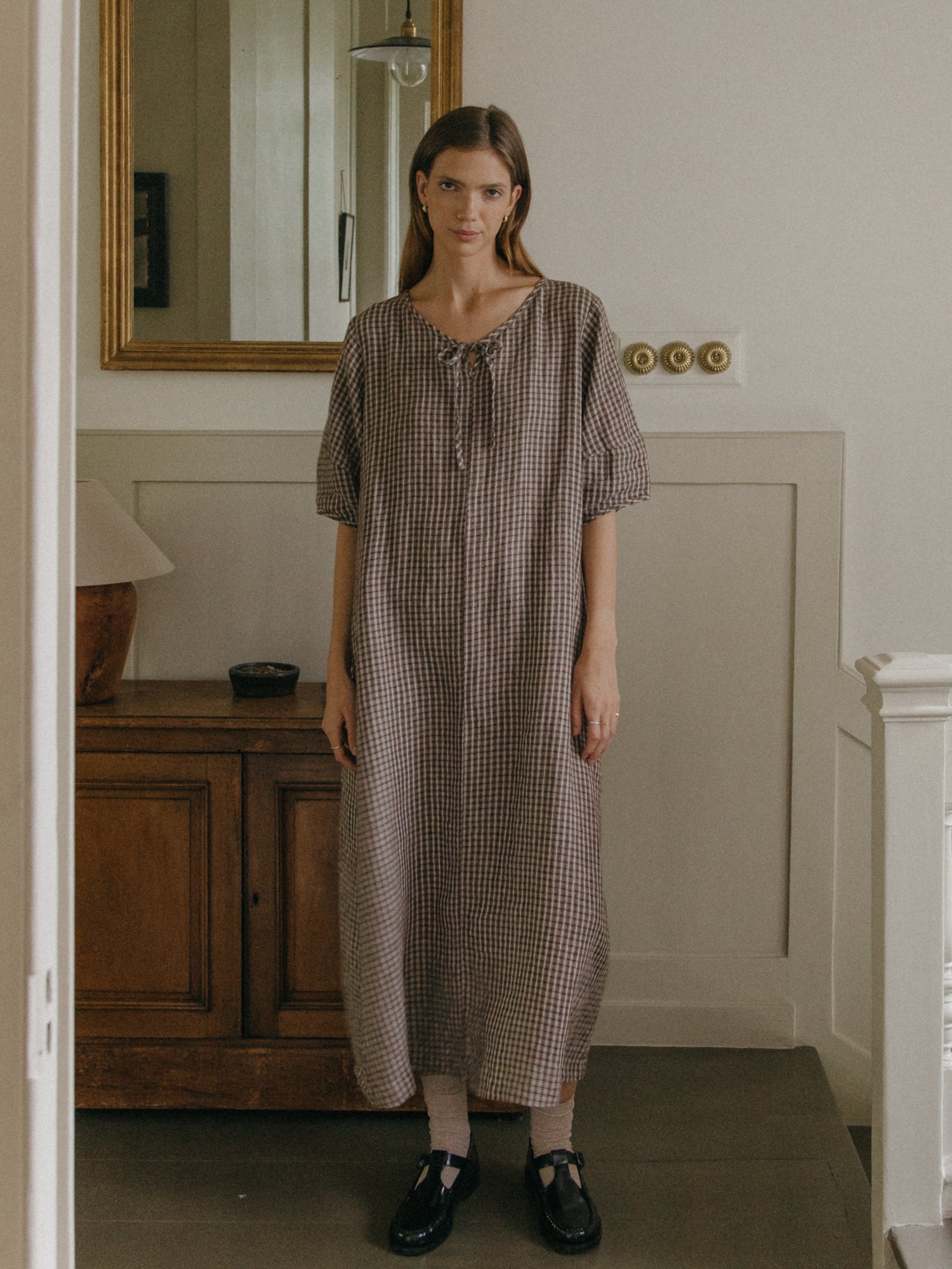 Model wearing the Blair Dress in Chocolate Plaid by Gillian Stevens, front view in a styled interior setting