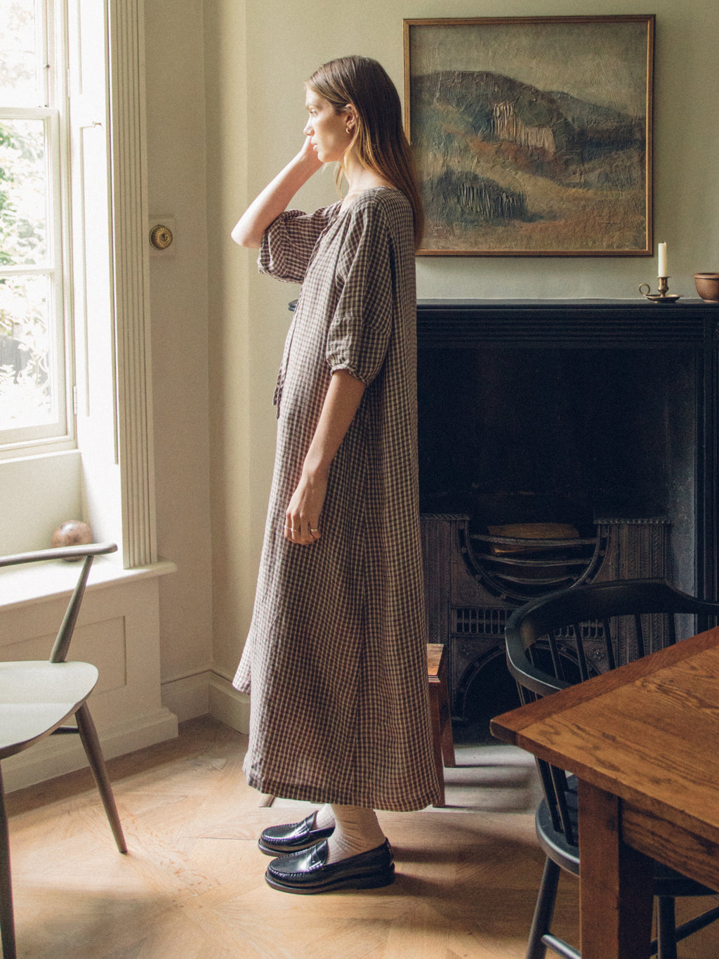 Model wearing the Blair Dress in Chocolate Plaid by Gillian Stevens, side view in a styled interior setting
