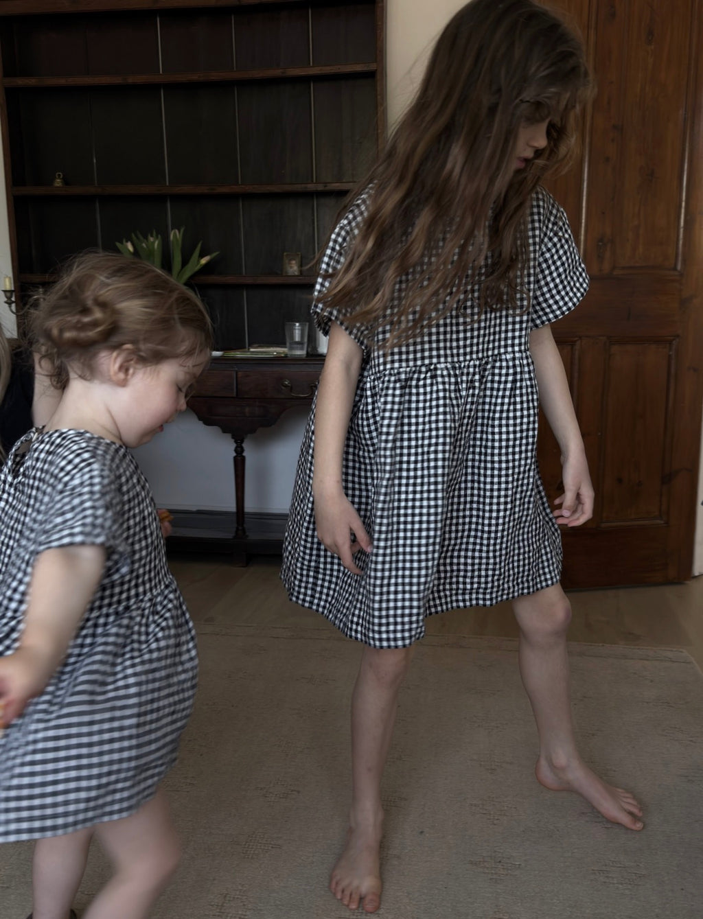 Two girls playing indoors in the Mini Aya Gingham in Noir by Gillian Stevens, showing movement and fit