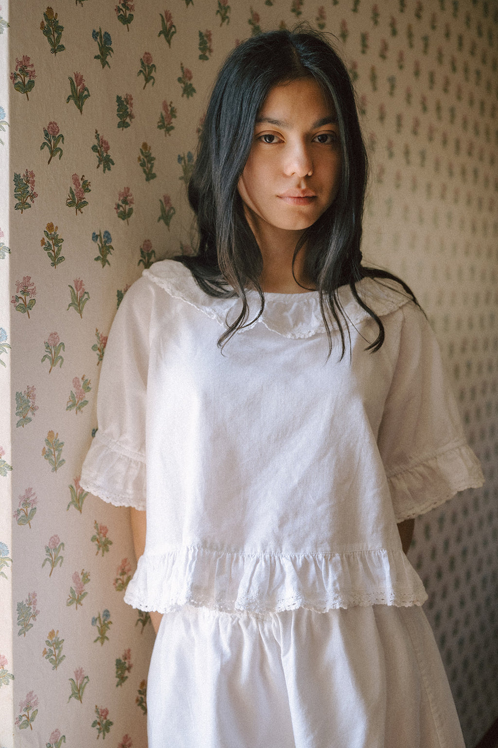 Model wearing the Arlette Top in Salt by Gillian Stevens, front view against floral wallpaper
