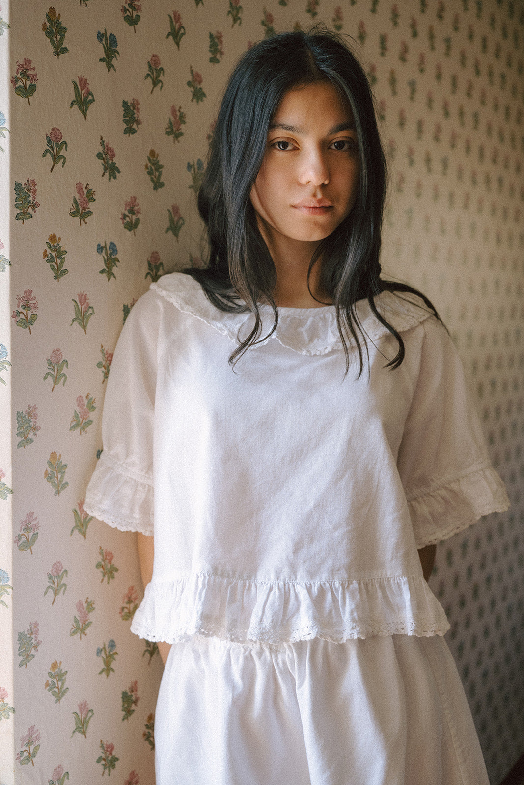 Model wearing the Arlette Top in Salt by Gillian Stevens, front view against floral wallpaper