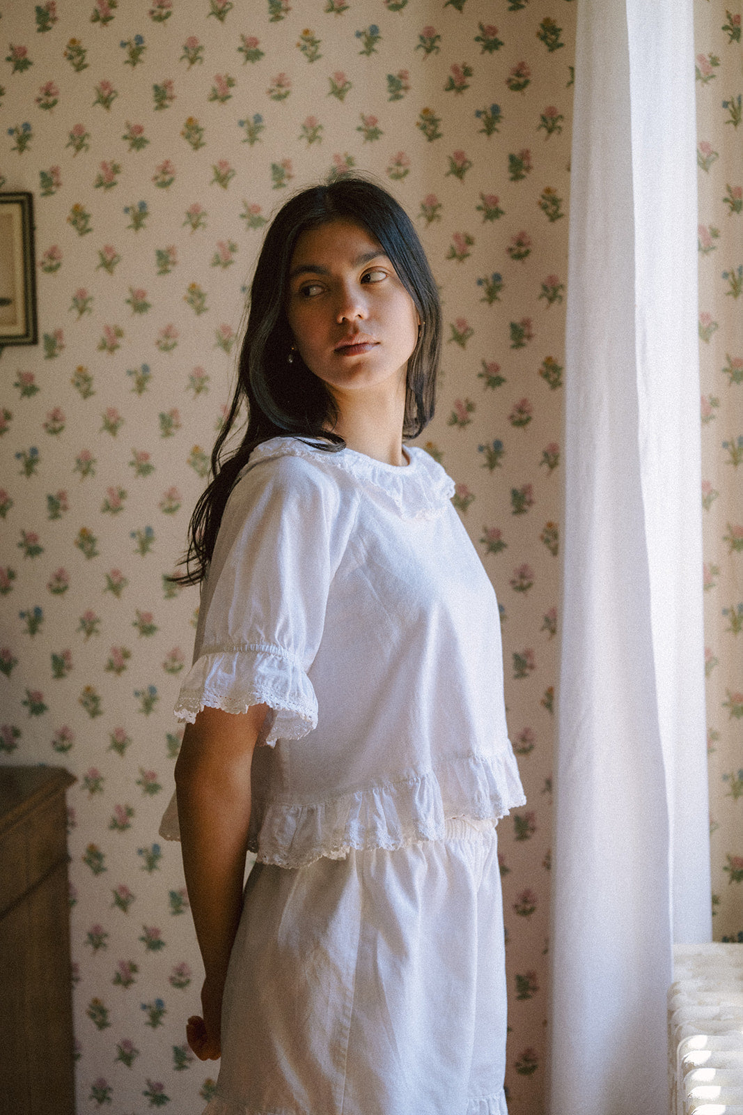 Model in the Arlette Top in Salt by Gillian Stevens, three-quarter view showing lace-trim sleeves and ruffle hem