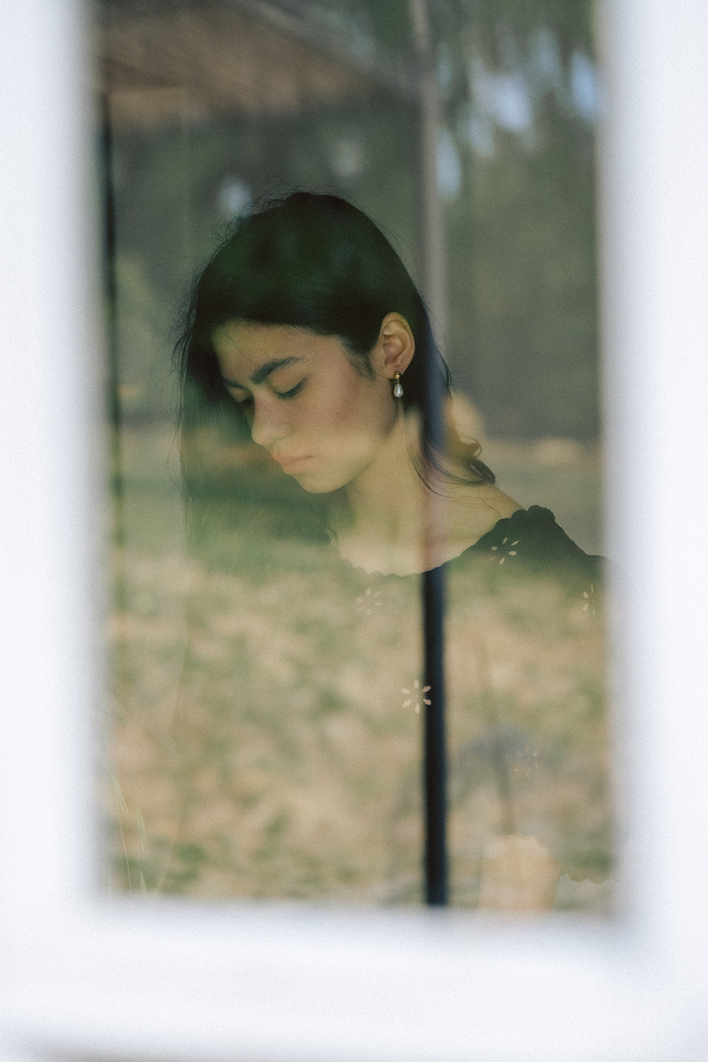 Model wearing the Stella Top in Noir by Gillian Stevens, portrait through a window with garden reflection