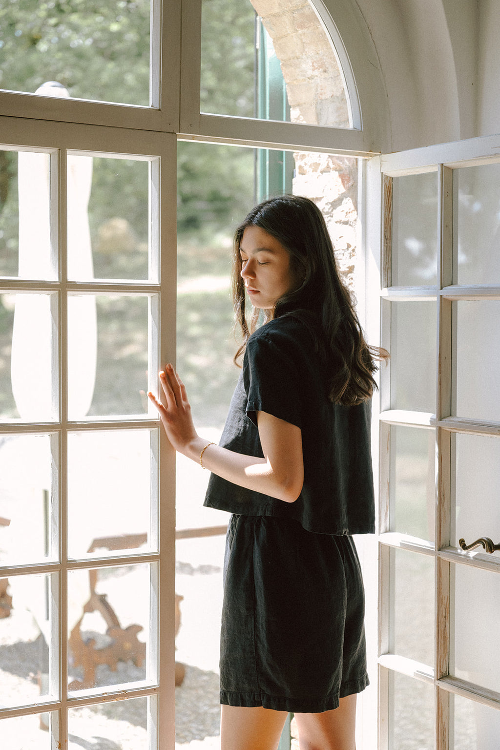Model wearing the Wren Top in Noir by Gillian Stevens, side view beside arched French doors