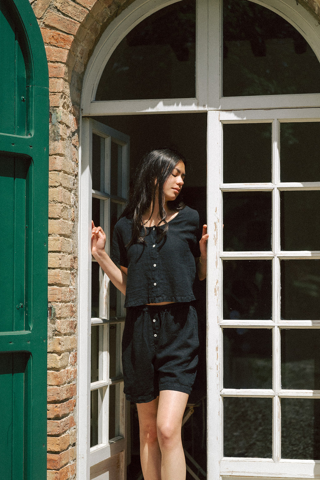 Model wearing the Wren Top in Noir by Gillian Stevens, front view in an arched doorway with brick surrounds