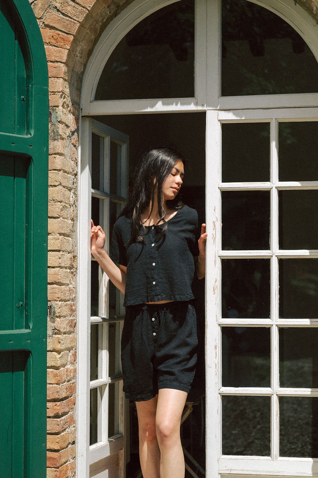 Model wearing the Wren Top in Noir by Gillian Stevens, front view in an arched doorway with brick surrounds