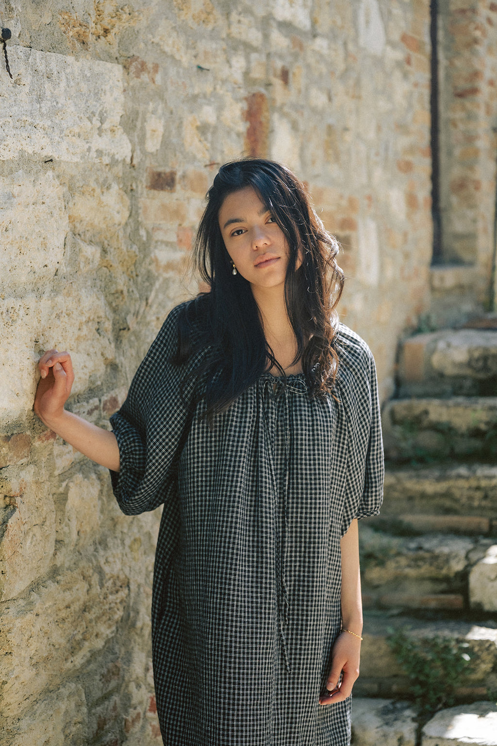 Model wearing the Jones Dress in Black Check by Gillian Stevens, front view against a stone wall