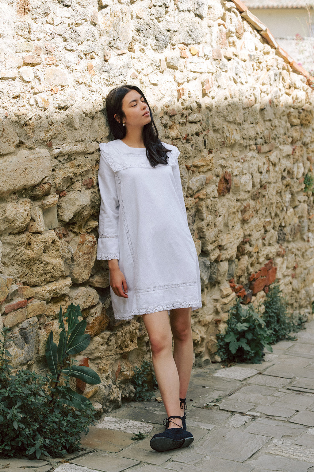 Model wearing the Laine Dress in Salt by Gillian Stevens, full-length front view against a rustic stone wall