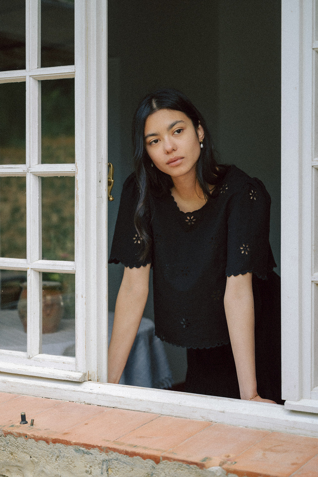 Model wearing the Stella Top in Noir by Gillian Stevens, front view framed in white French doors
