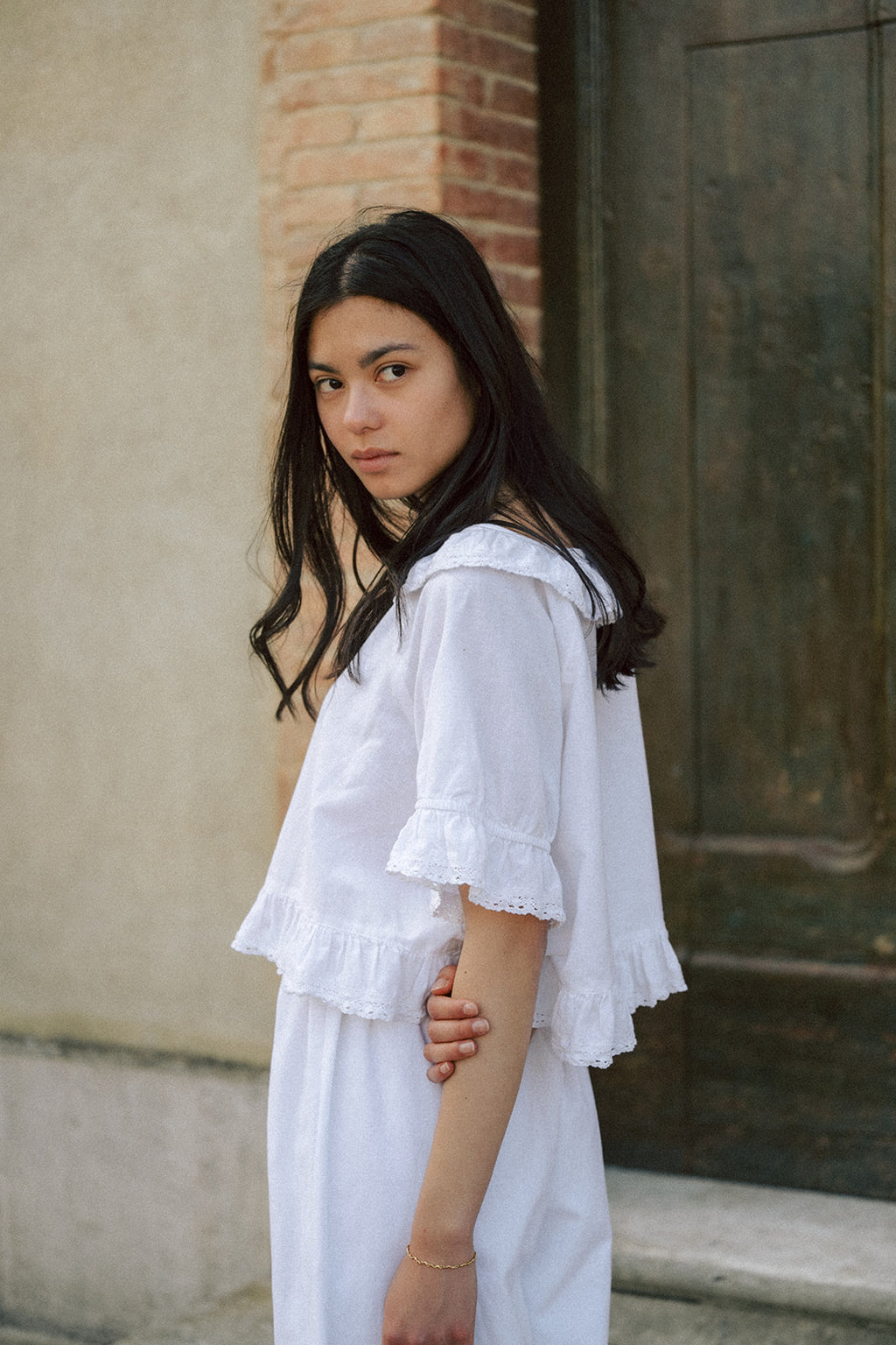 Model in the Arlette Top in Salt by Gillian Stevens, three-quarter side view showing ruffle hem and lace trim detail
