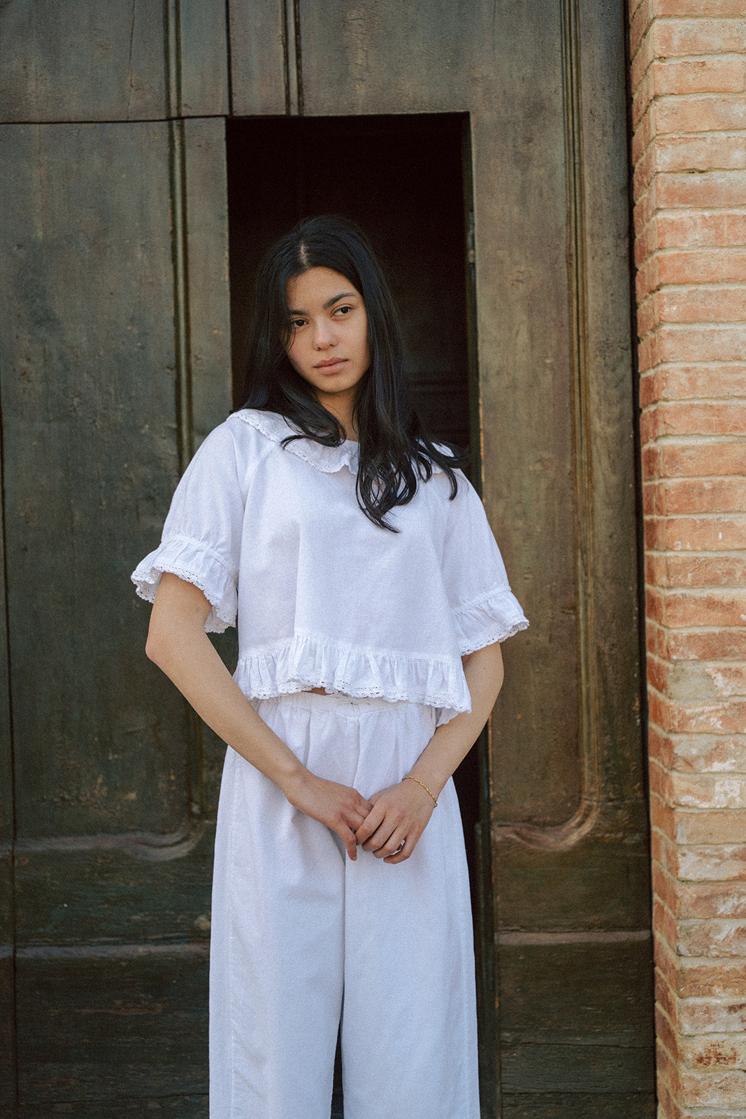Model wearing the Arlette Top in Salt by Gillian Stevens, front view against a rustic brick and timber doorway