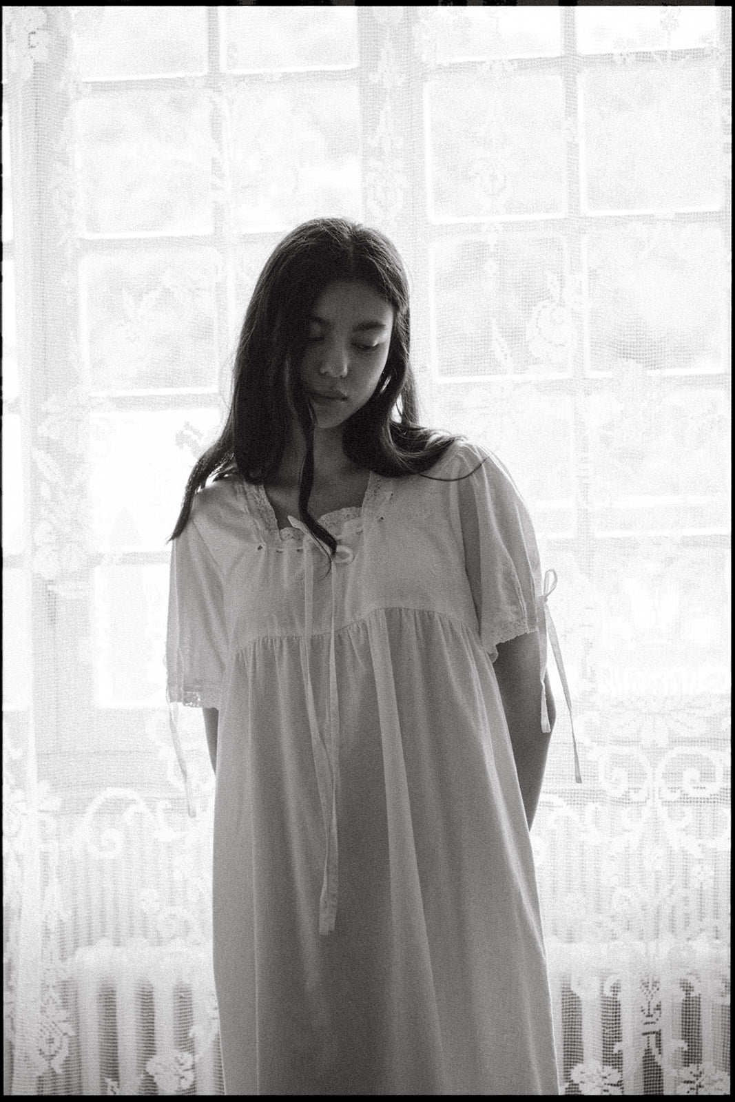 Model wearing the Dace Dress in Salt by Gillian Stevens, front view by a lace-curtained window