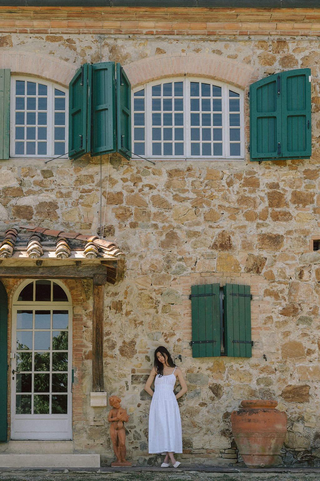 Model wearing the Alessandra Dress in Salt by Gillian Stevens, full-length front view against a rustic Tuscan stone villa