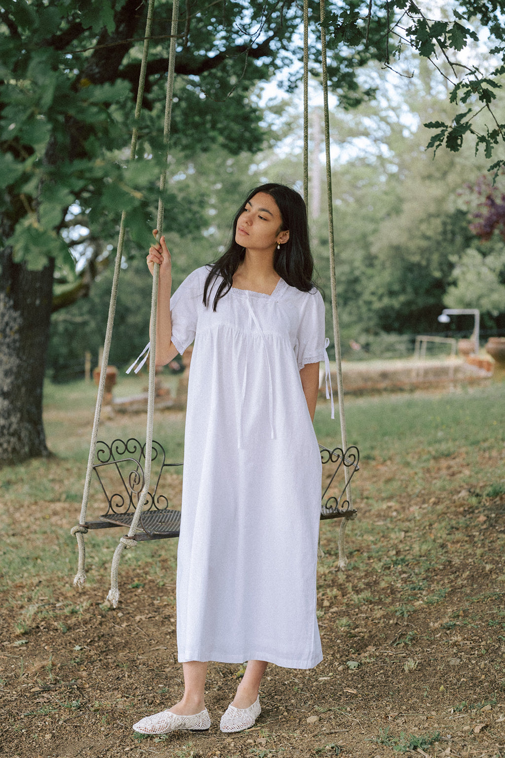 Model wearing the Dace Dress in Salt by Gillian Stevens, front view beside a garden swing