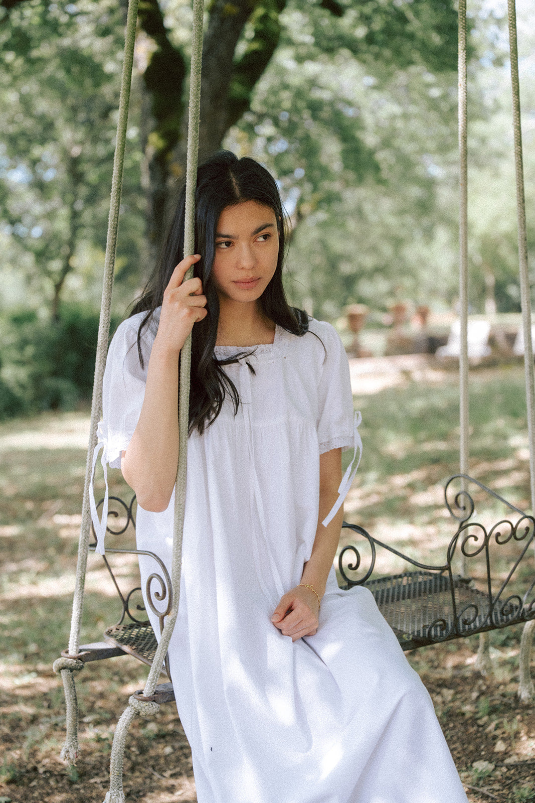 Model seated on a garden swing wearing the Dace Dress in Salt by Gillian Stevens, front view