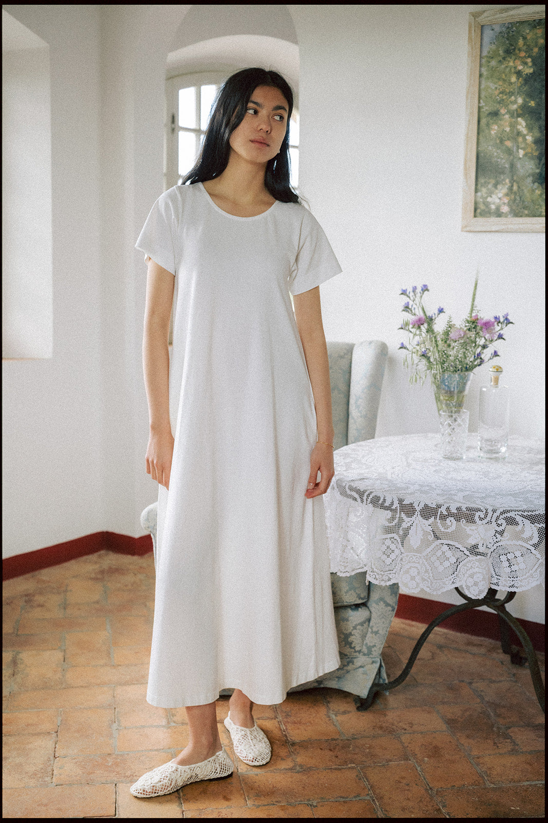 Model wearing the Palmer Dress in Salt by Gillian Stevens, three-quarter view in a rustic interior setting