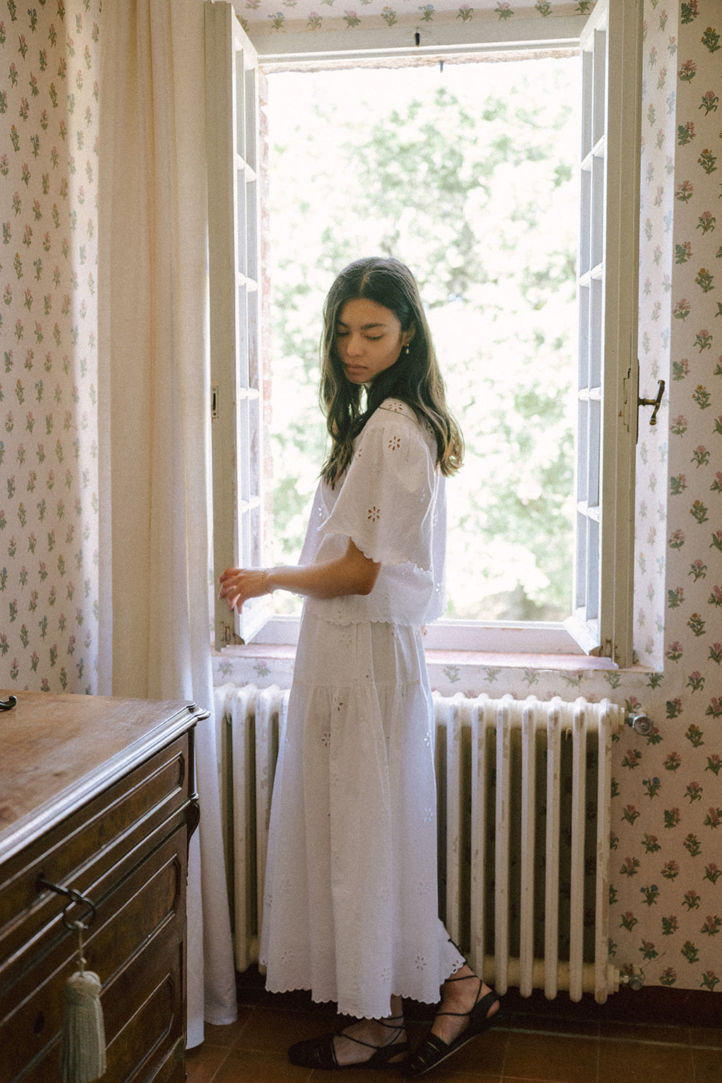 Model wearing the Stella Top in Salt by Gillian Stevens, side view by an open window in a floral room