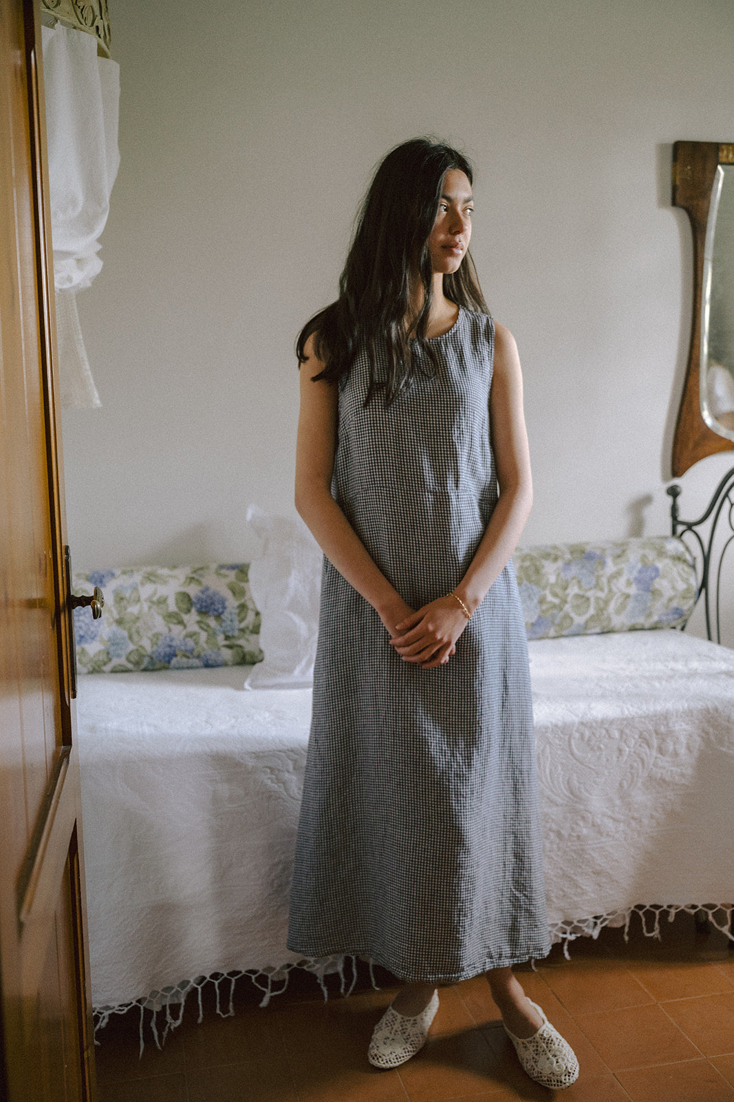 Model wearing the Paige Dress in Marine Gingham by Gillian Stevens, full-length front view in a bedroom setting