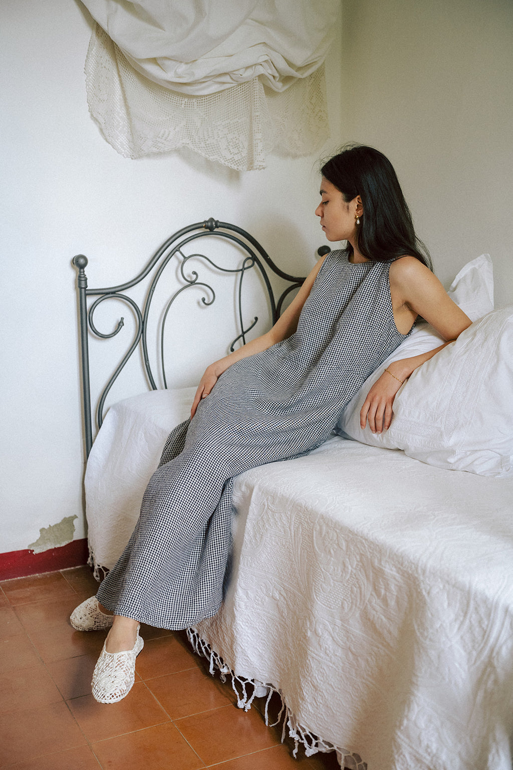 Model seated on a bed in the Paige Dress in Marine Gingham by Gillian Stevens, side profile view