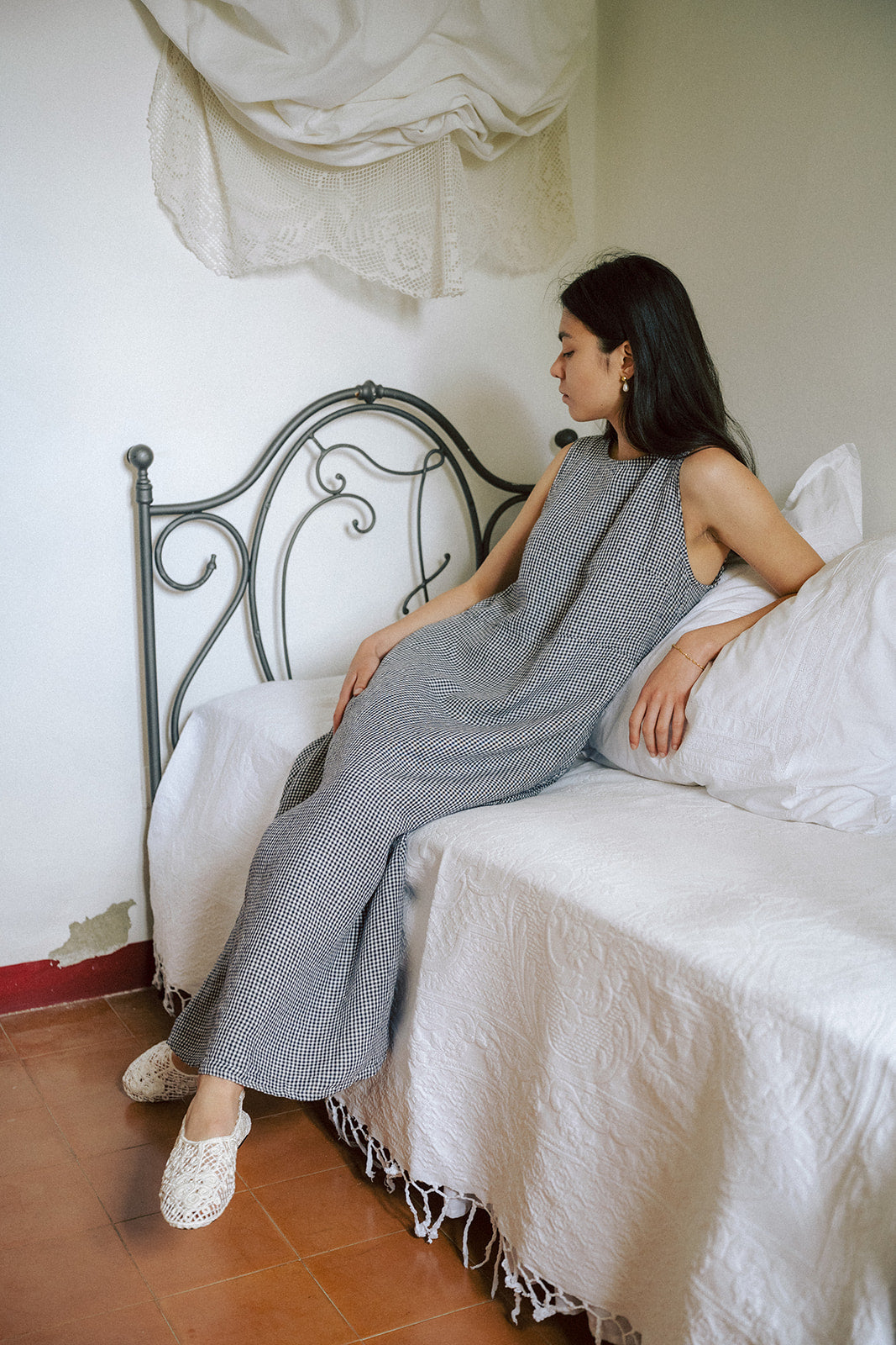 Model seated on a bed in the Paige Dress in Marine Gingham by Gillian Stevens, side profile view