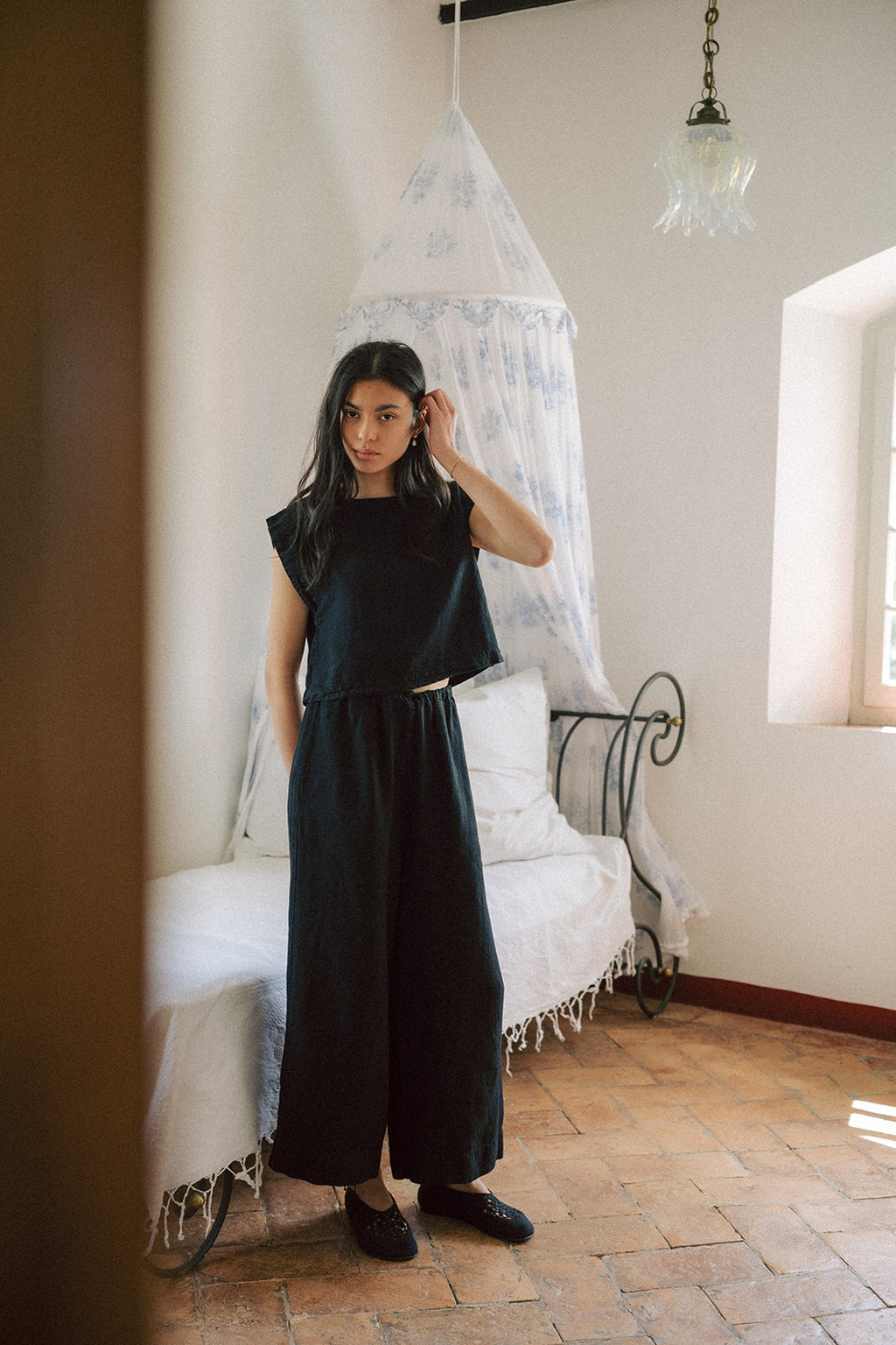 Model wearing the Ines Pant in Noir by Gillian Stevens, full-length front view in a sunlit room