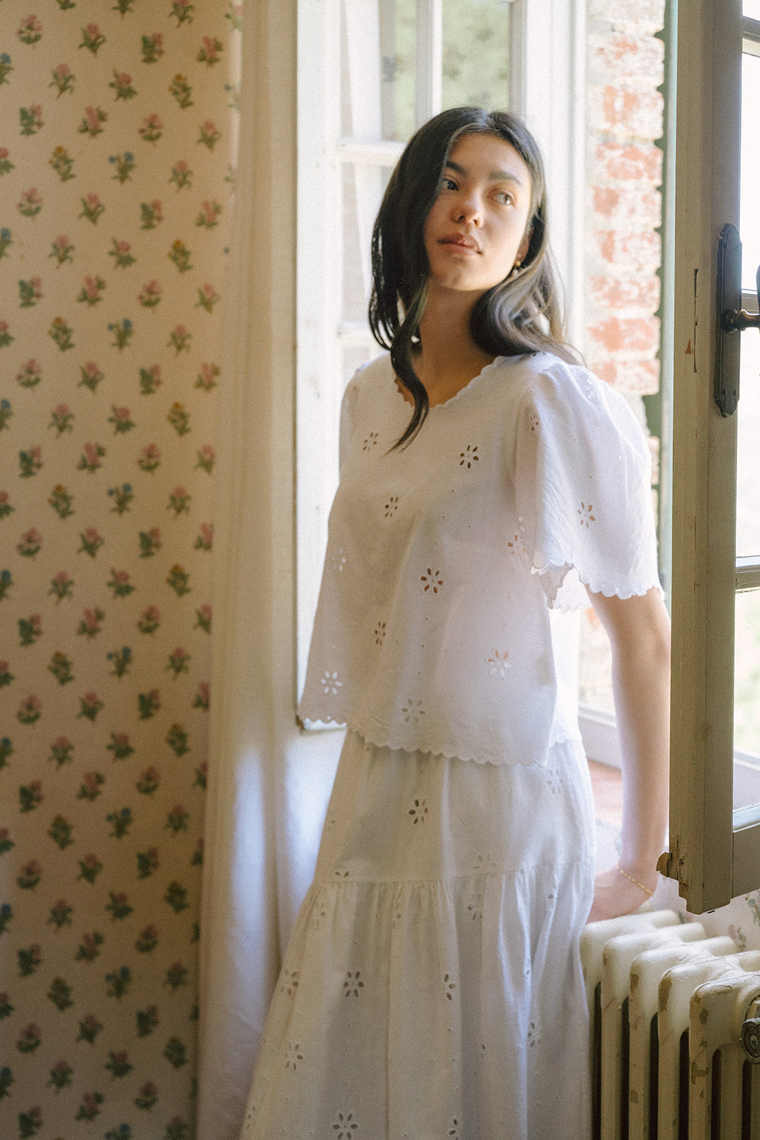 Model wearing the Stella Top in Salt by Gillian Stevens, three-quarter view beside a window with floral wallpaper