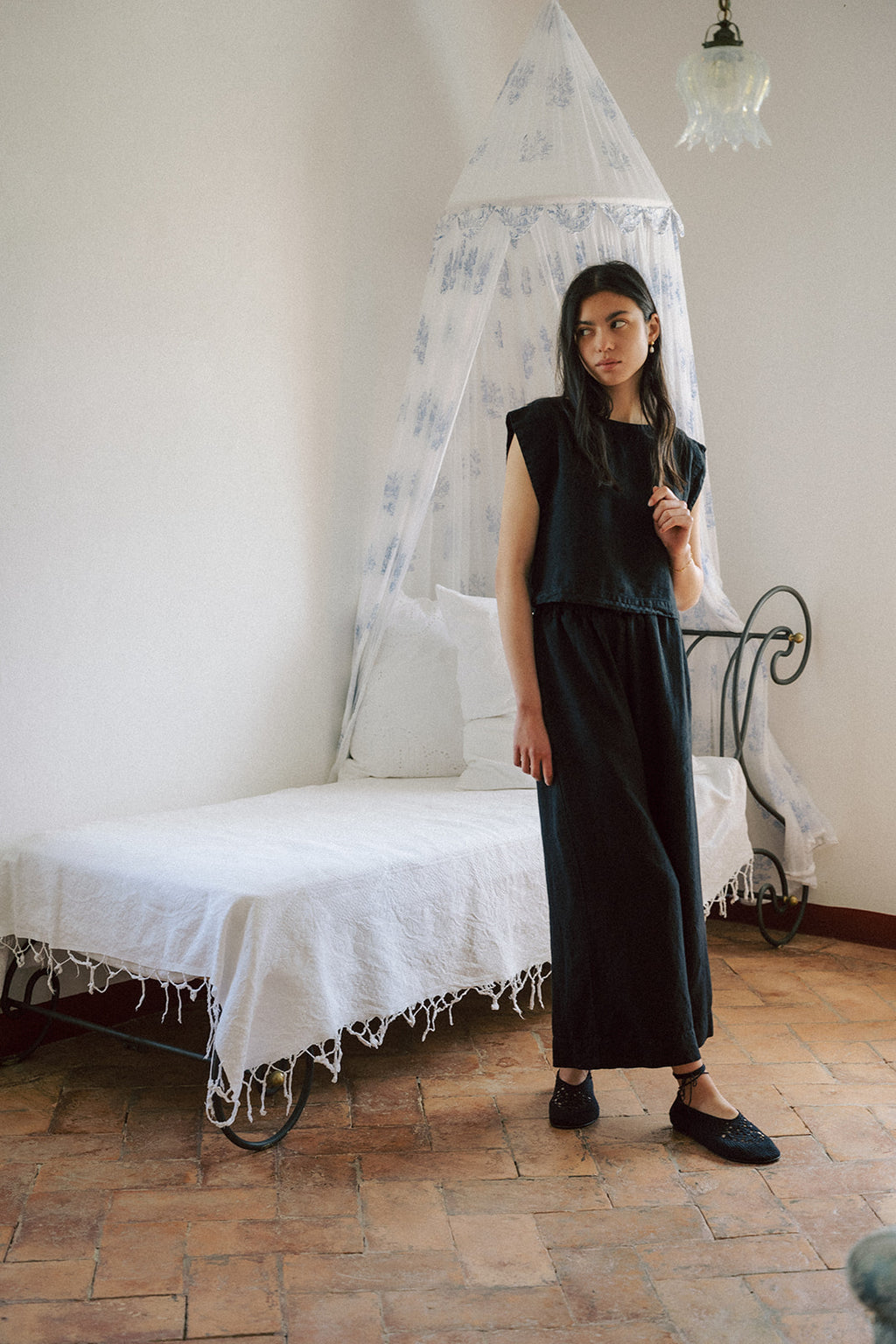 Model wearing the Ines Pant in Noir by Gillian Stevens, full-length front view in a styled bedroom setting
