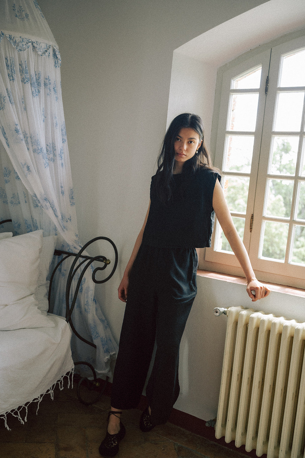 Model wearing the Ines Pant in Noir by Gillian Stevens, full-length front view in a sunlit vintage room