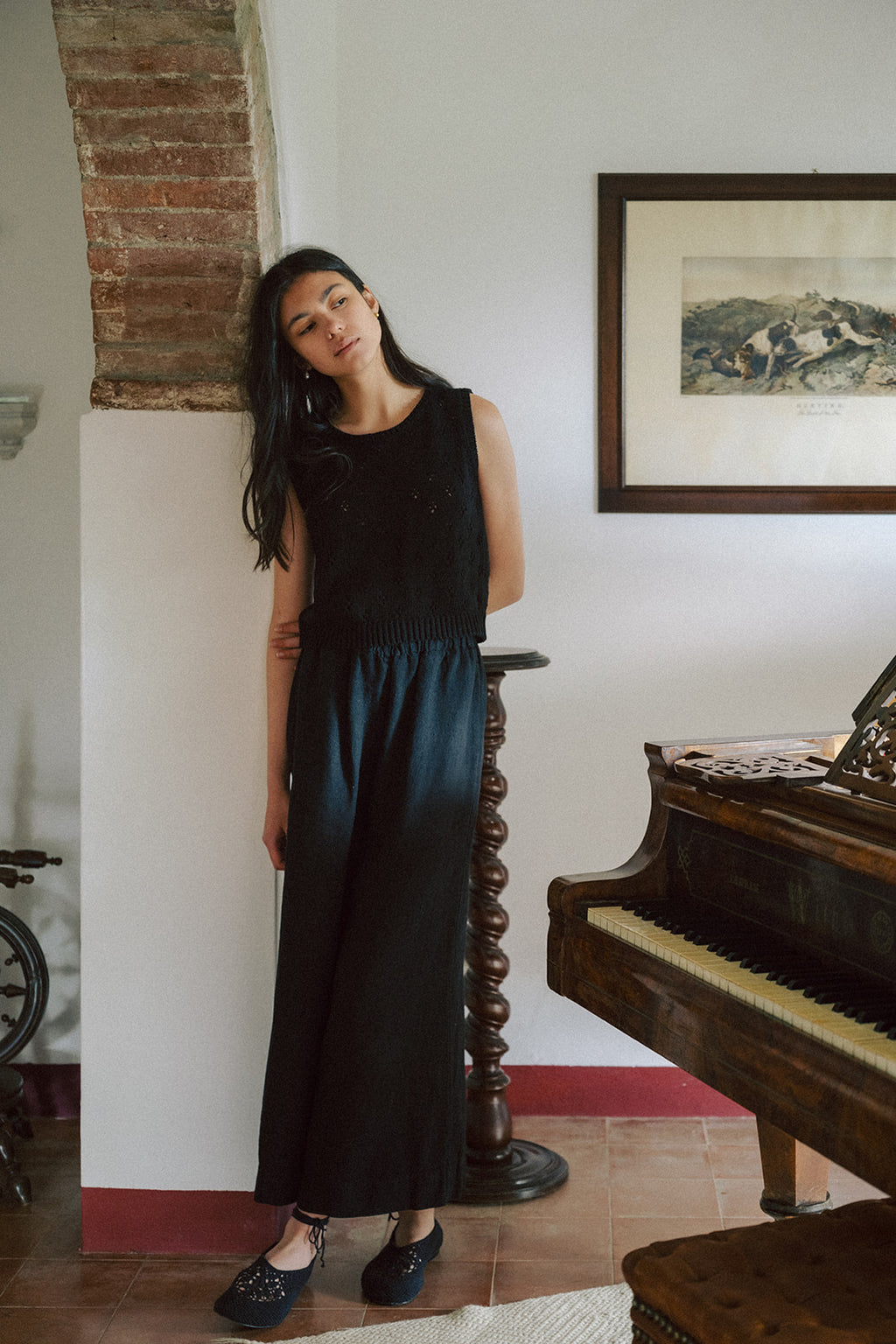 Model wearing the Niah Top in Noir by Gillian Stevens, full-length front view beside a grand piano