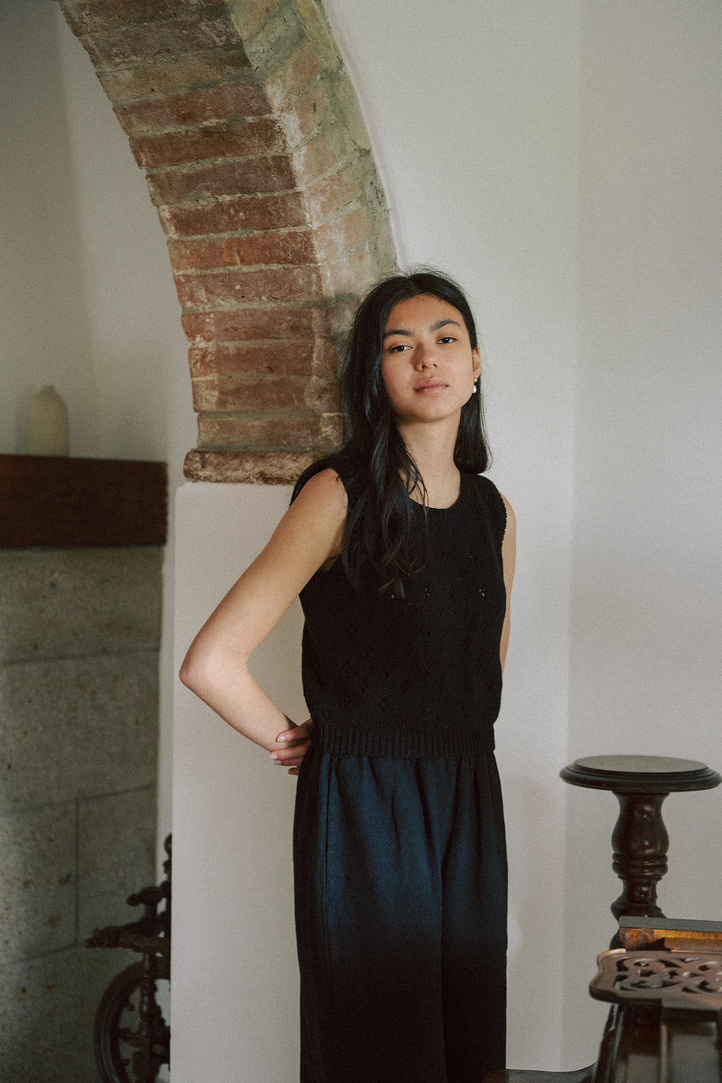 Model wearing the Niah Top in Noir by Gillian Stevens, front view beside a rustic brick arch
