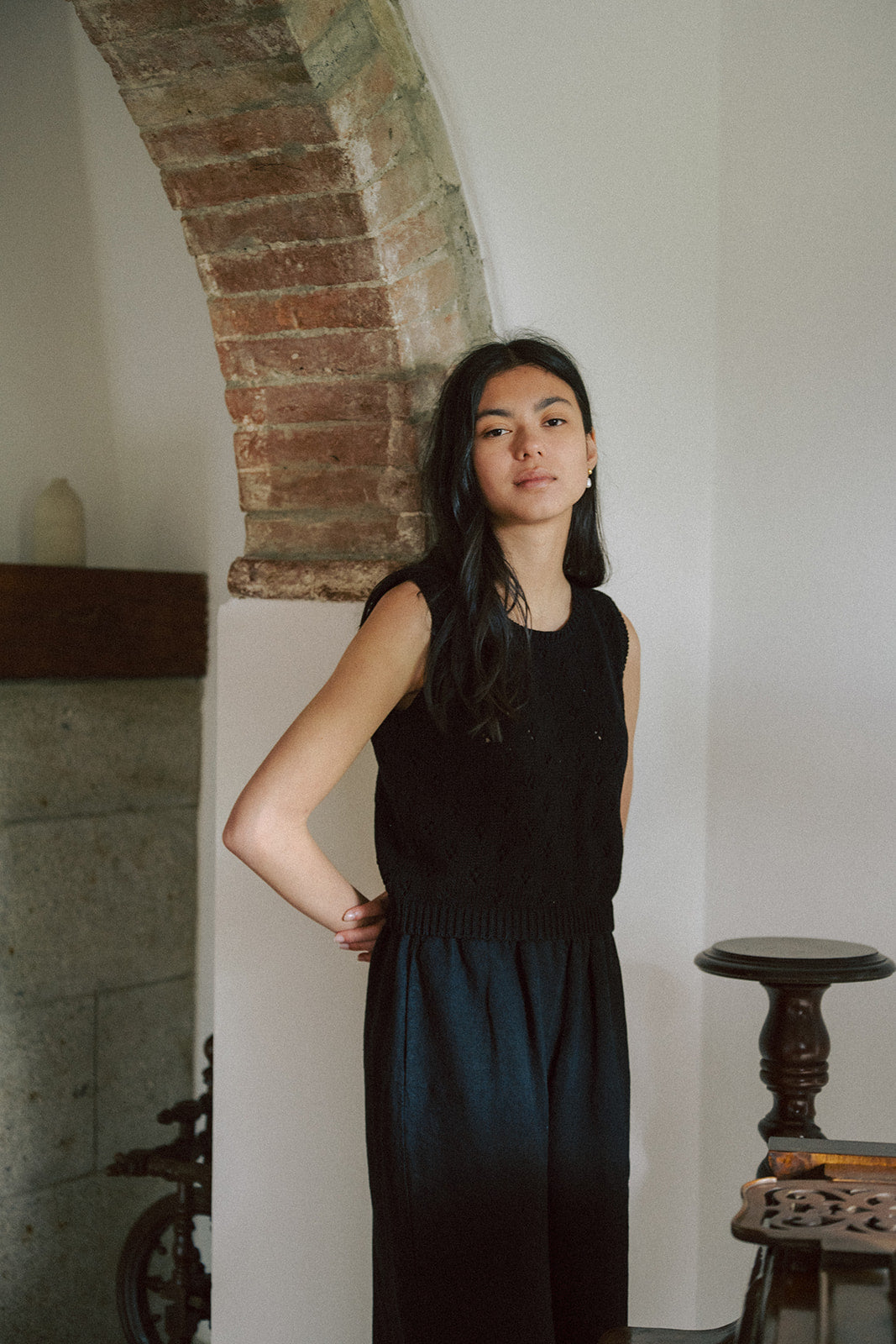 Model wearing the Niah Top in Noir by Gillian Stevens, front view beside a rustic brick arch
