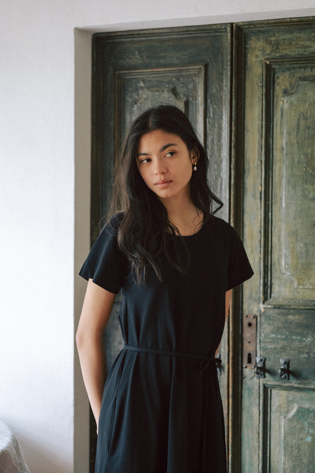 Model wearing the Palmer Dress in Noir by Gillian Stevens, front view beside a vintage door