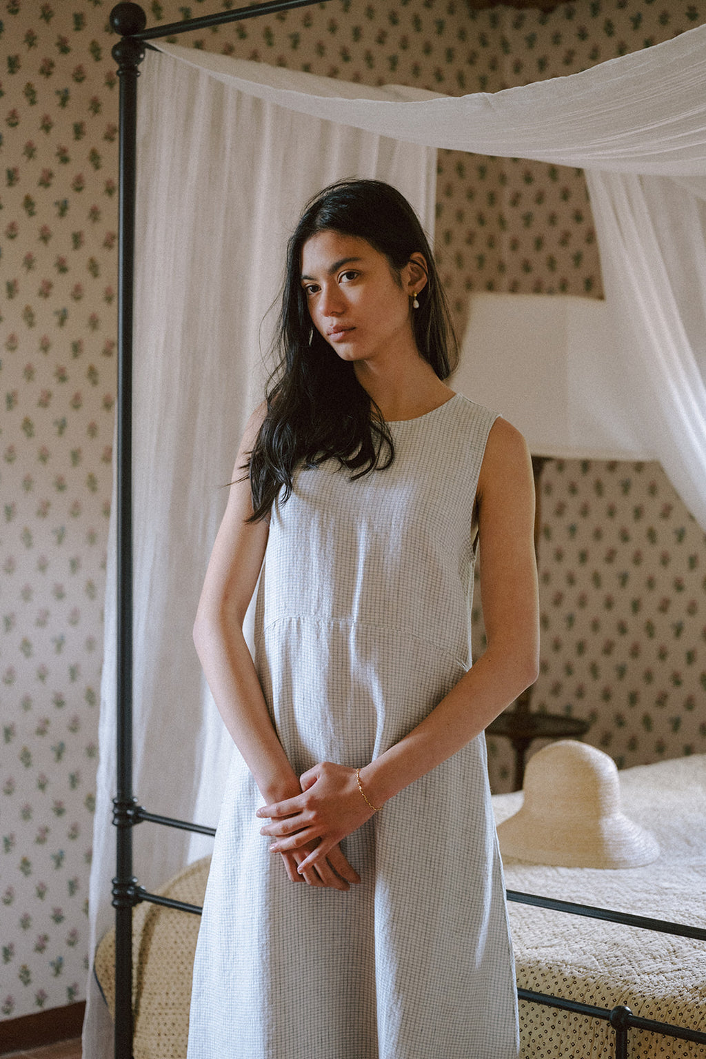 Model wearing the Paige Dress in Dusty Blue Plaid by Gillian Stevens, front view in a floral bedroom setting