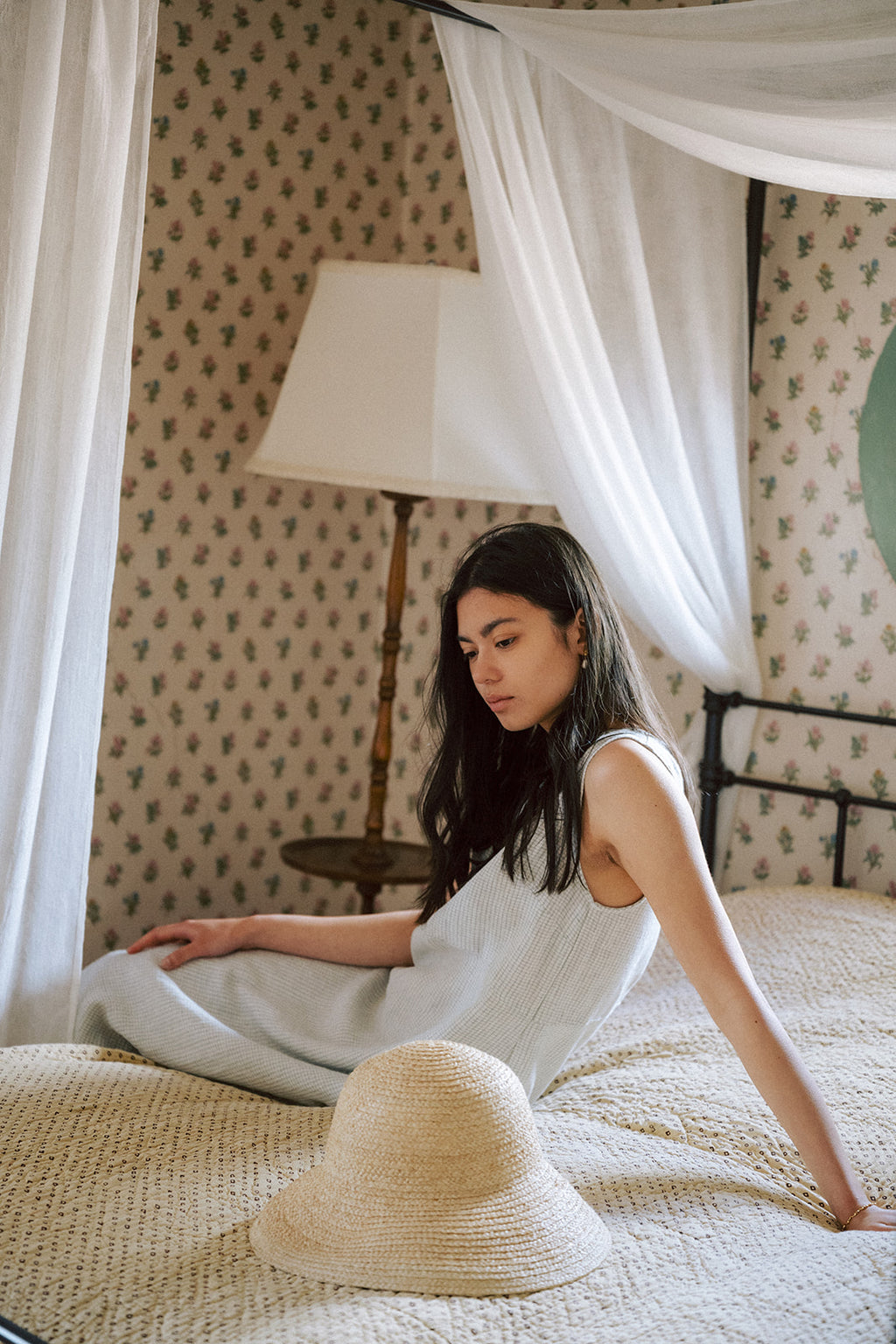 Model seated on a canopy bed wearing the Paige Dress in Dusty Blue Plaid by Gillian Stevens