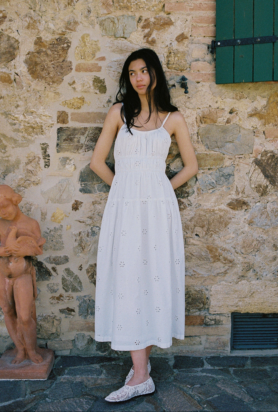 Model wearing the Alessandra Dress in Salt by Gillian Stevens, front view against a rustic stone wall