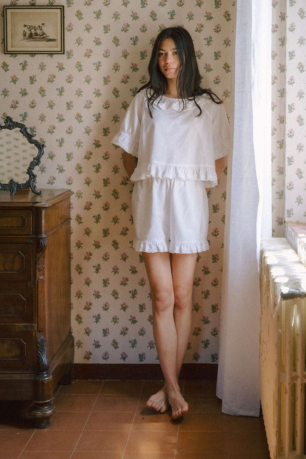 Model wearing the Arlette Short in Salt by Gillian Stevens, front view in a vintage floral bedroom setting